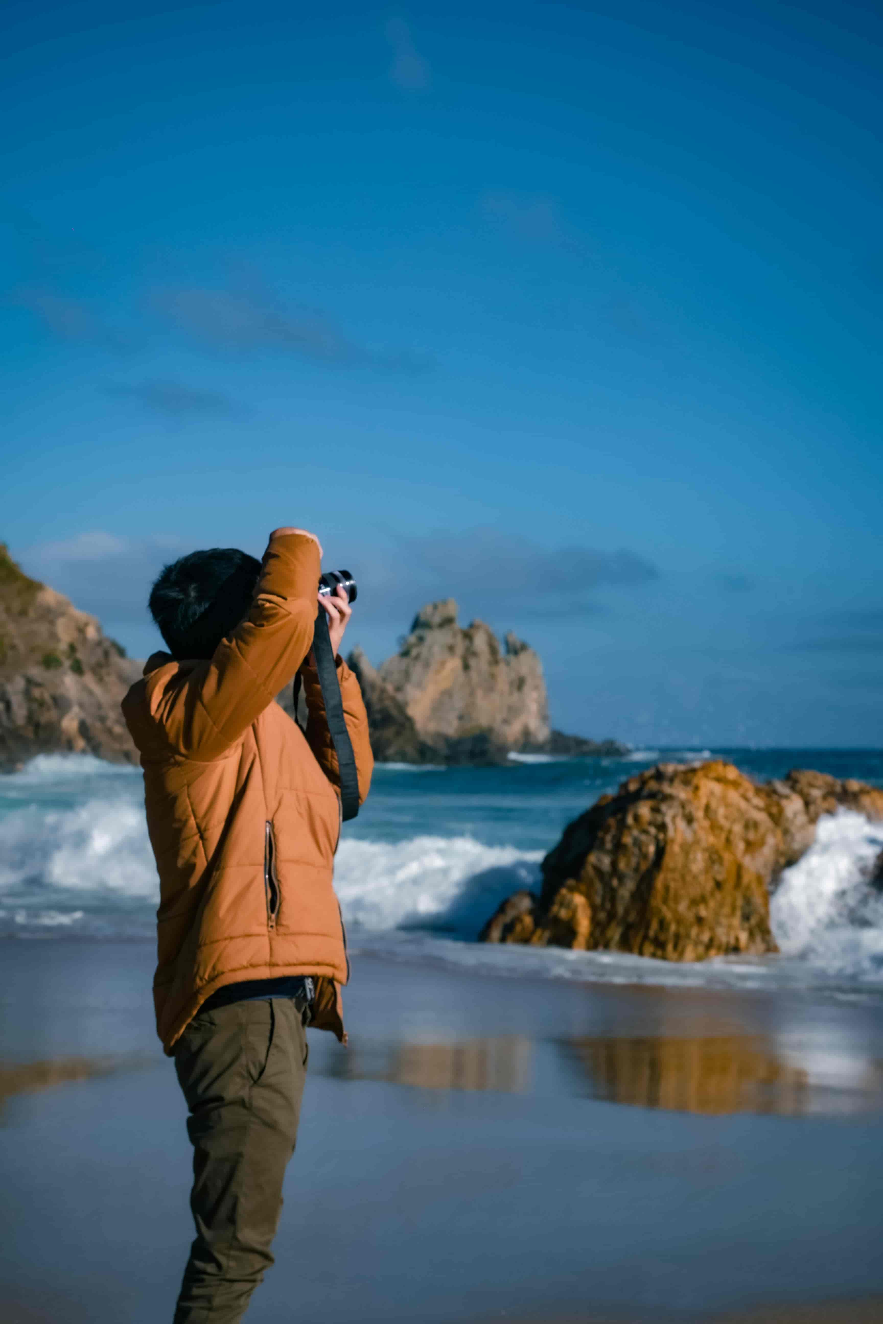 Photographer in an orange jacket shooting rugged sea stacks and crashing surf on a wet beach