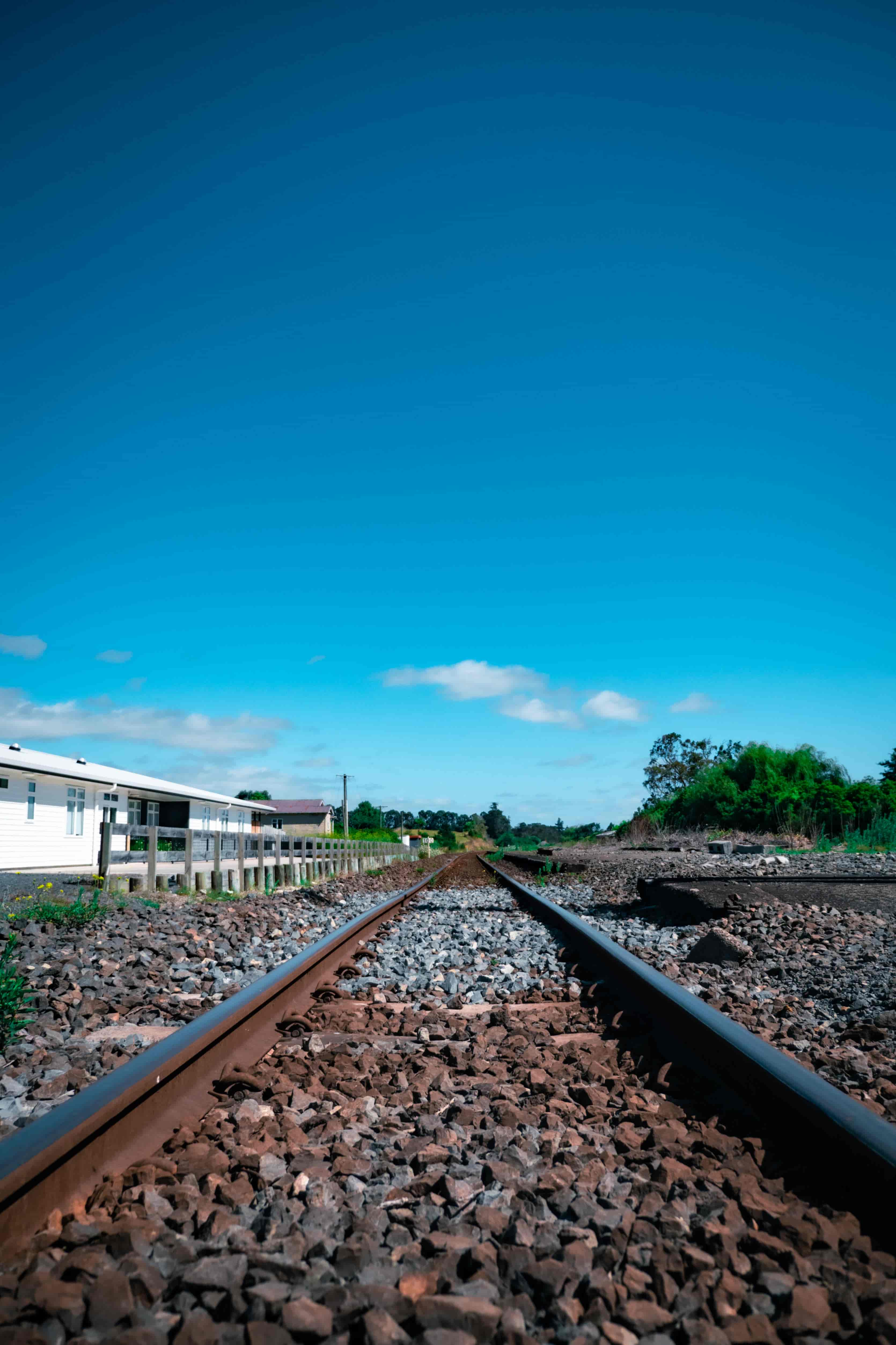 Low view along rusty railway tracks and gravel ballast stretching to the horizon under blue sky