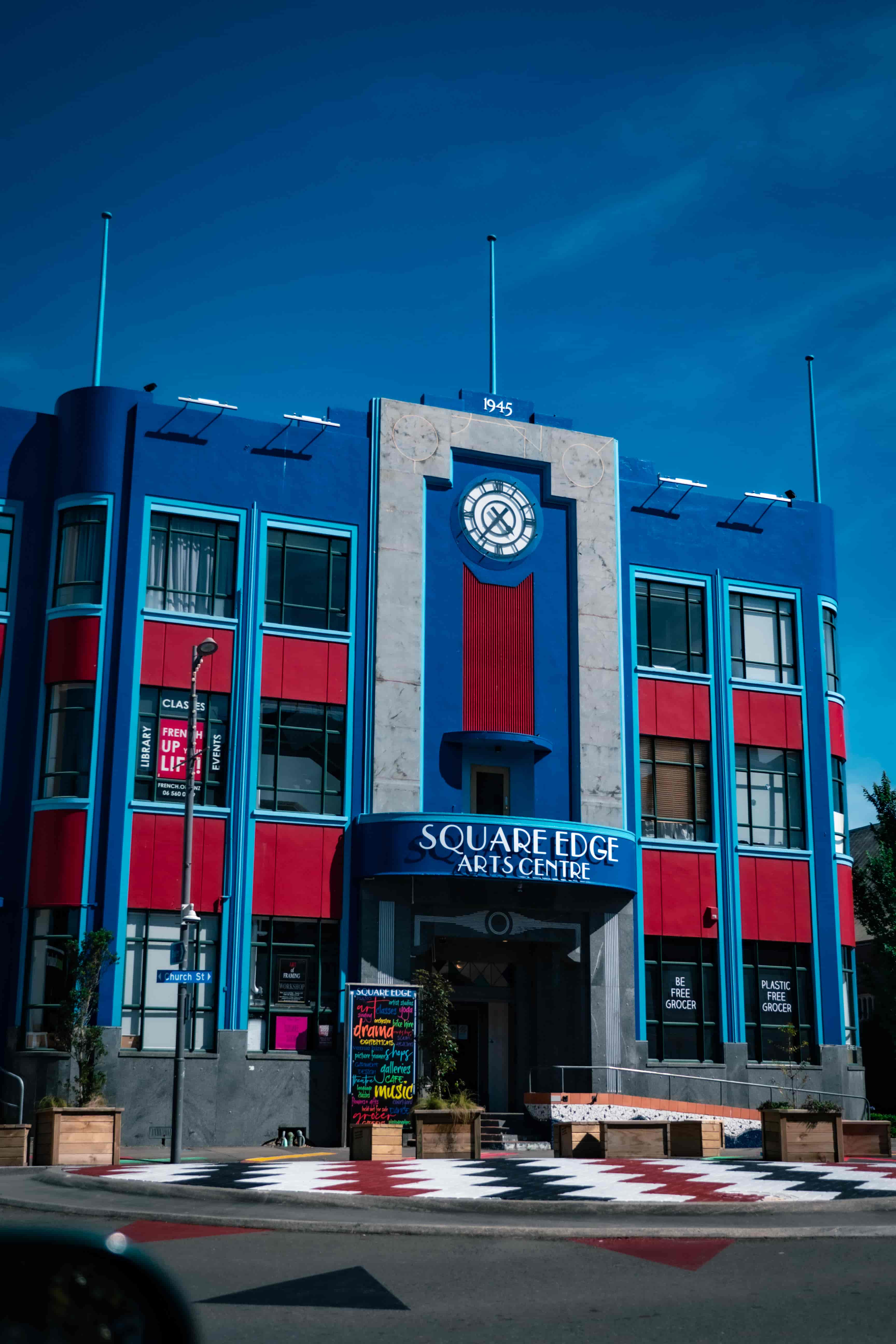 Blue and red Art Deco facade of the Square Edge Arts Centre with a clock emblem under a deep blue sky