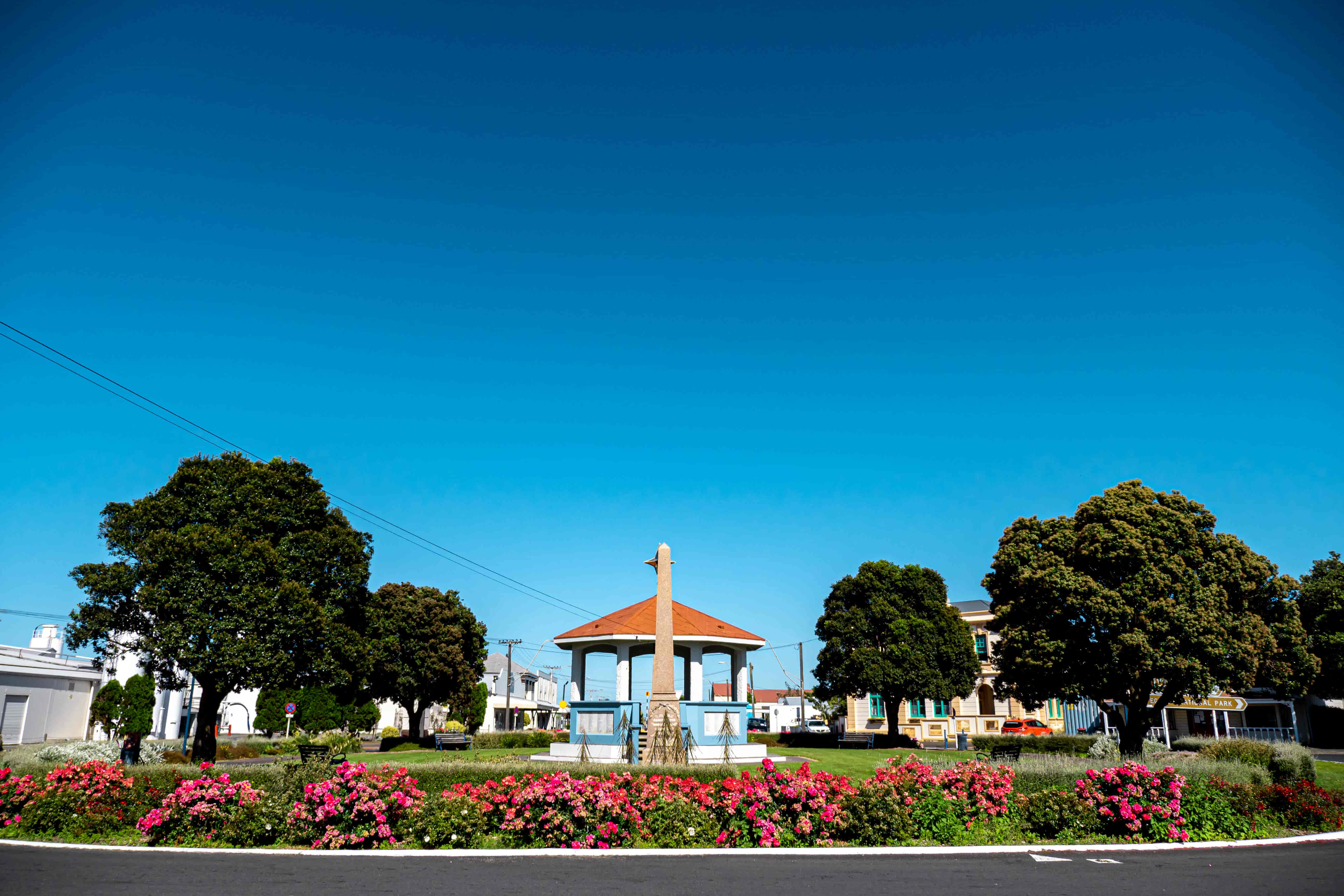 Town square with a memorial column, a red-roofed rotunda and pink rose beds under clear blue sky