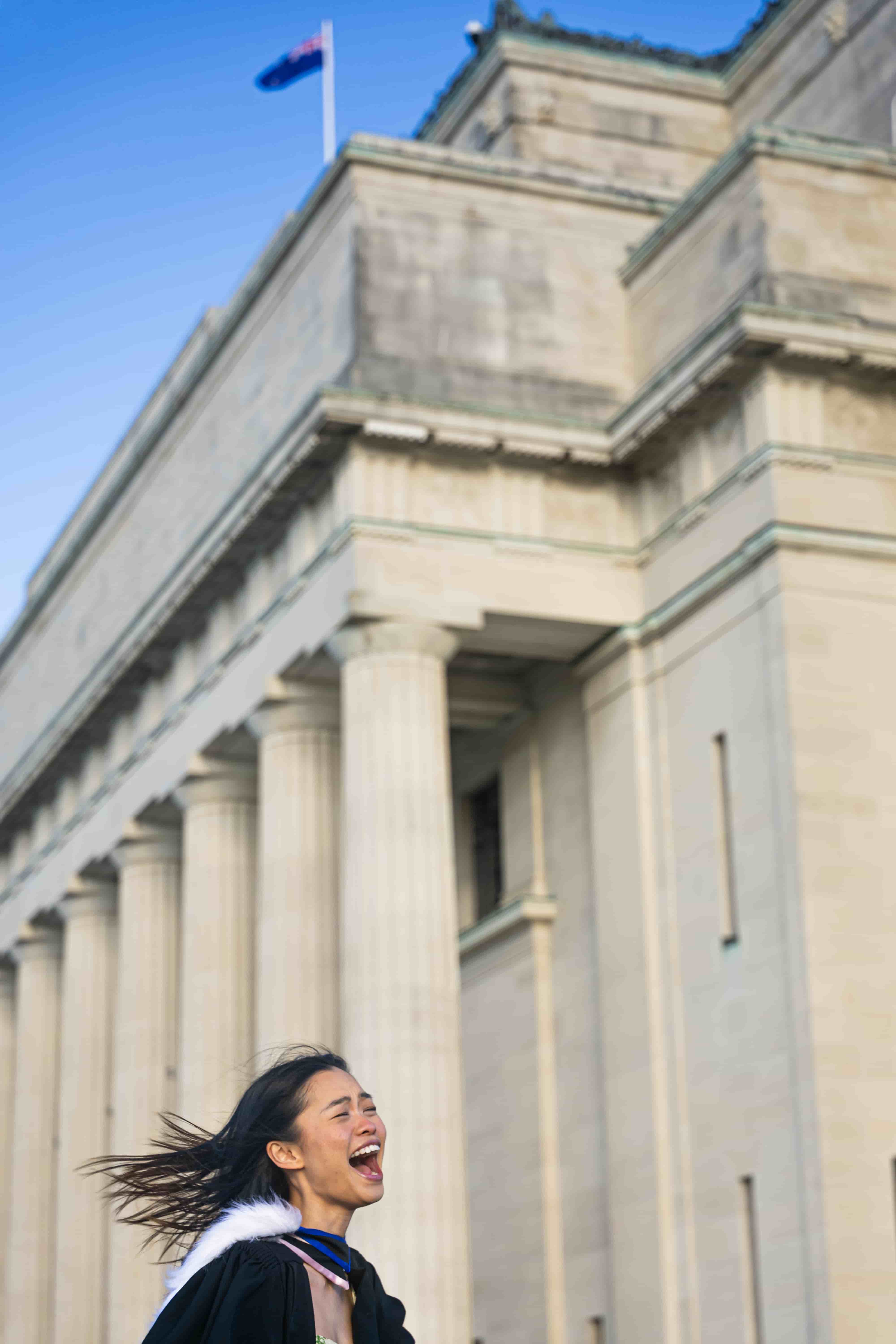 Ruby laughing below the columns of Auckland War Memorial Museum under a blue sky