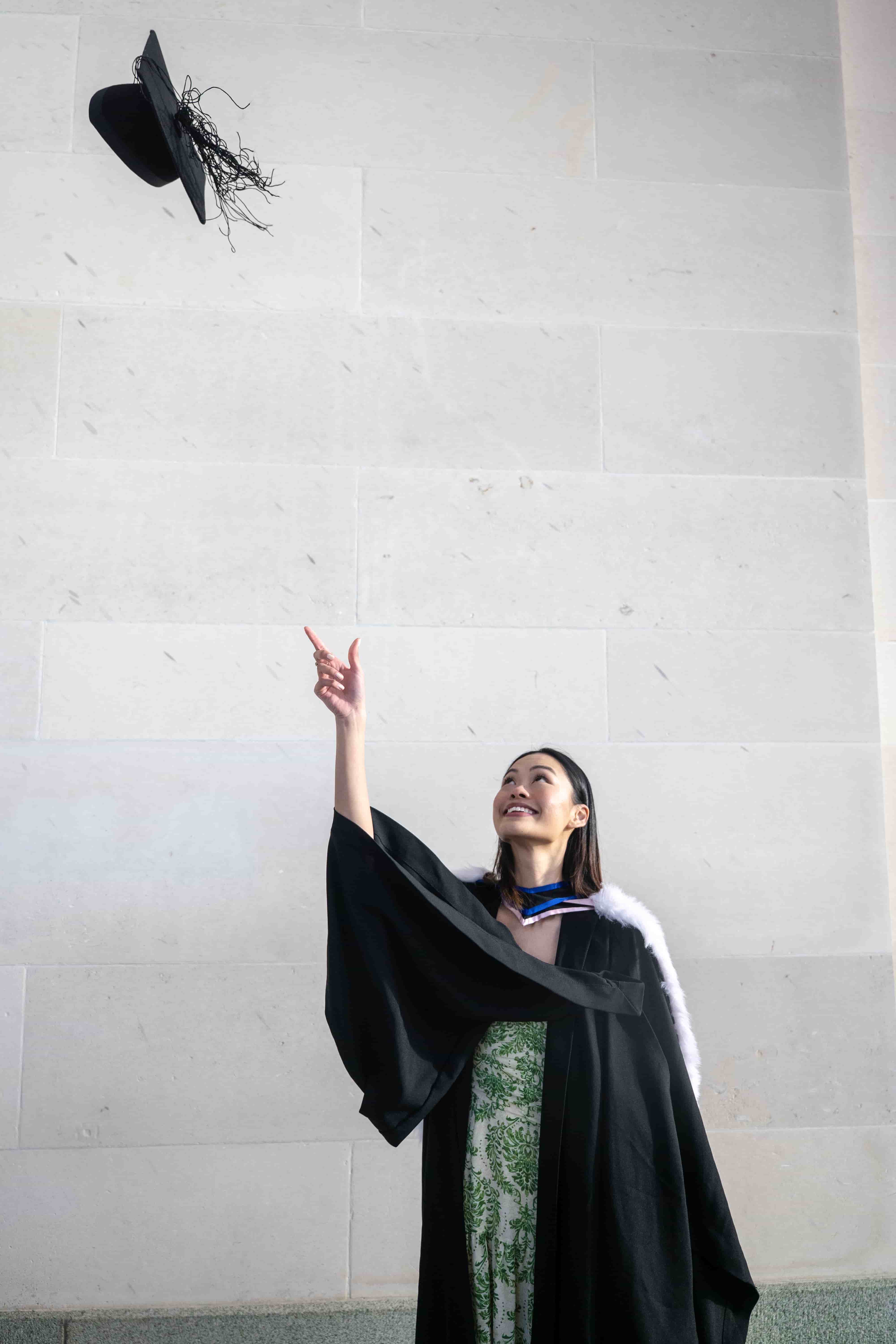 Ruby tossing her graduation cap into the air in front of a pale stone wall