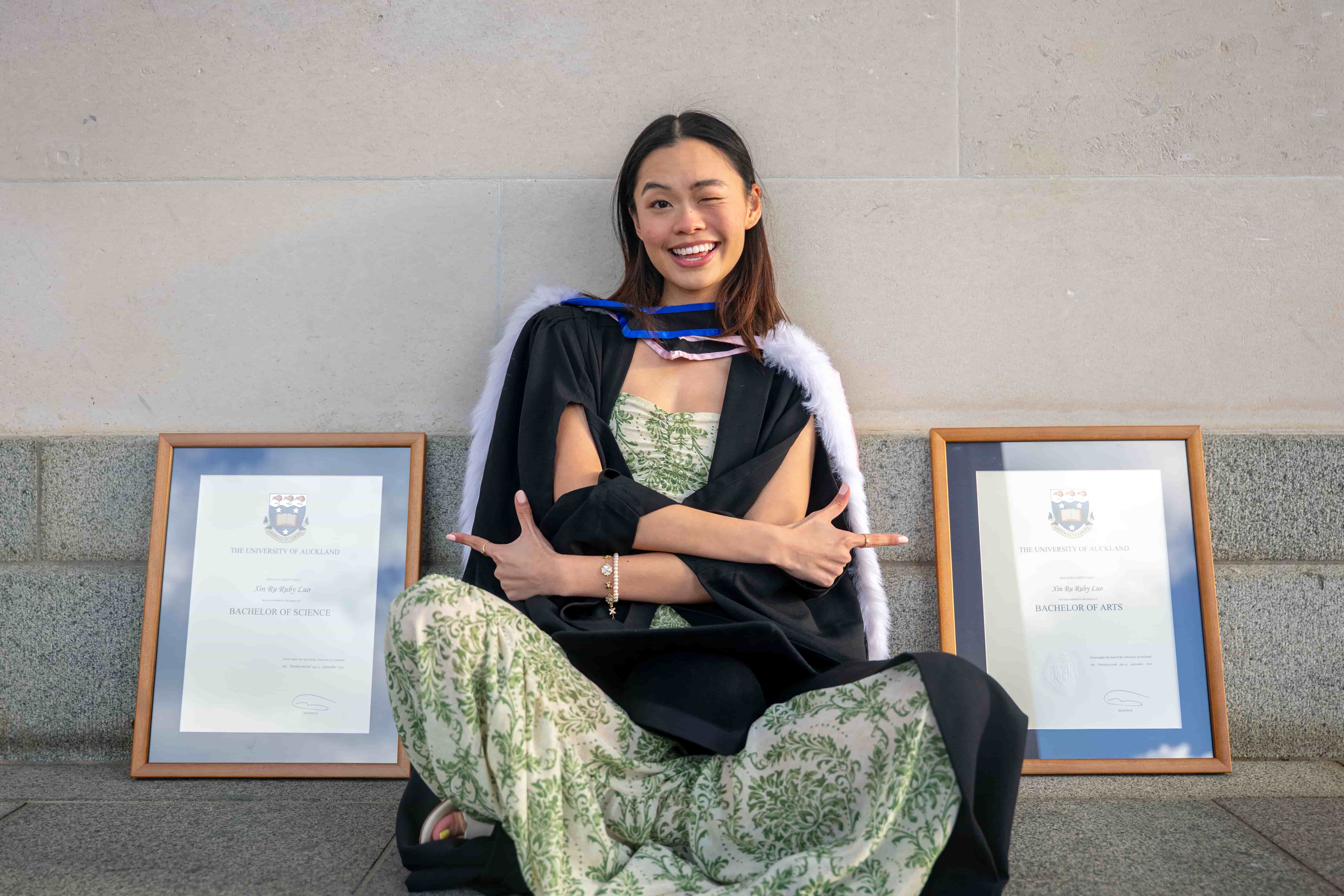 Ruby laughing while seated between her Bachelor of Arts and Bachelor of Science frames