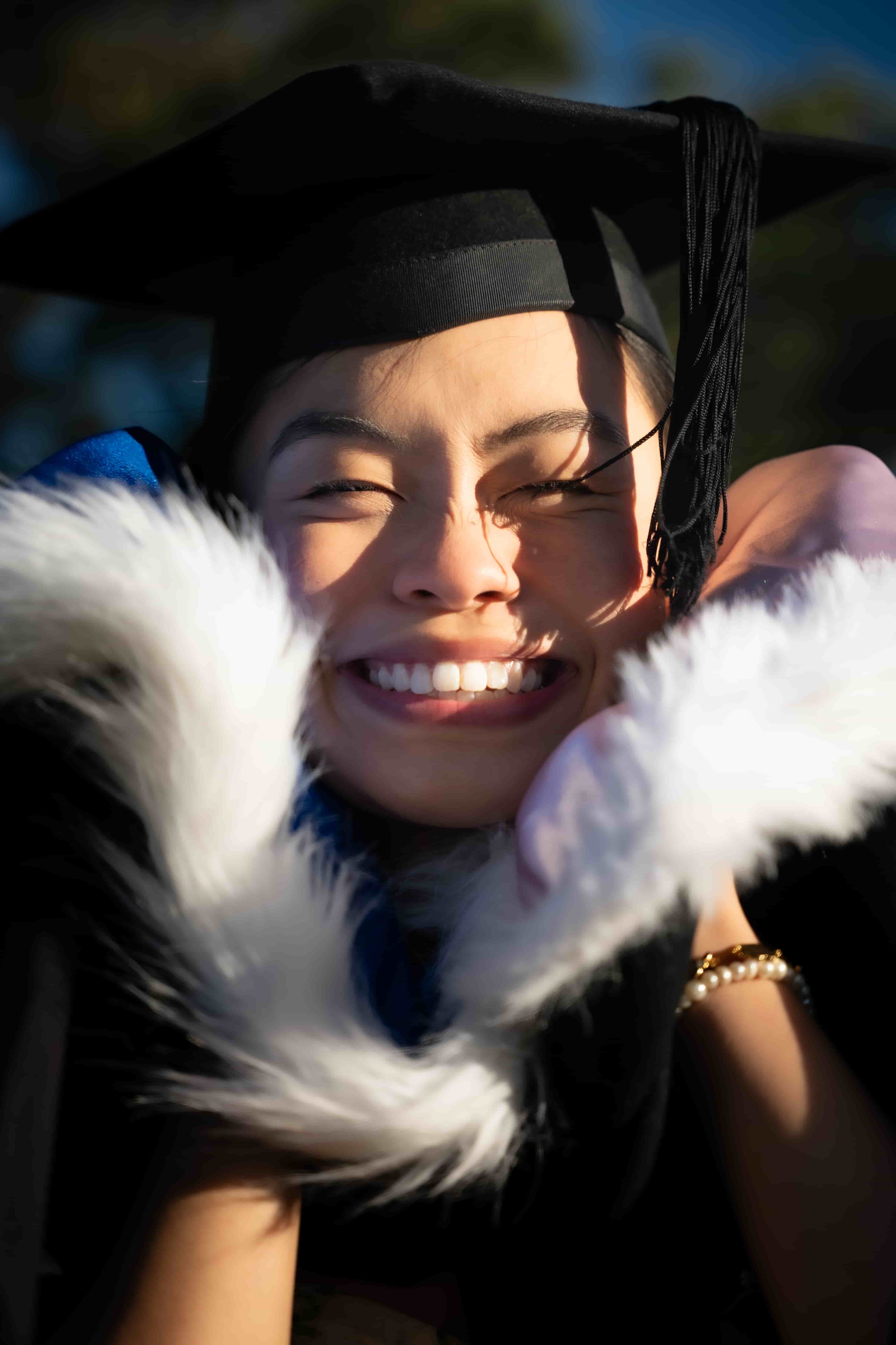 Ruby beaming in her graduation cap with the hood pulled up around her face