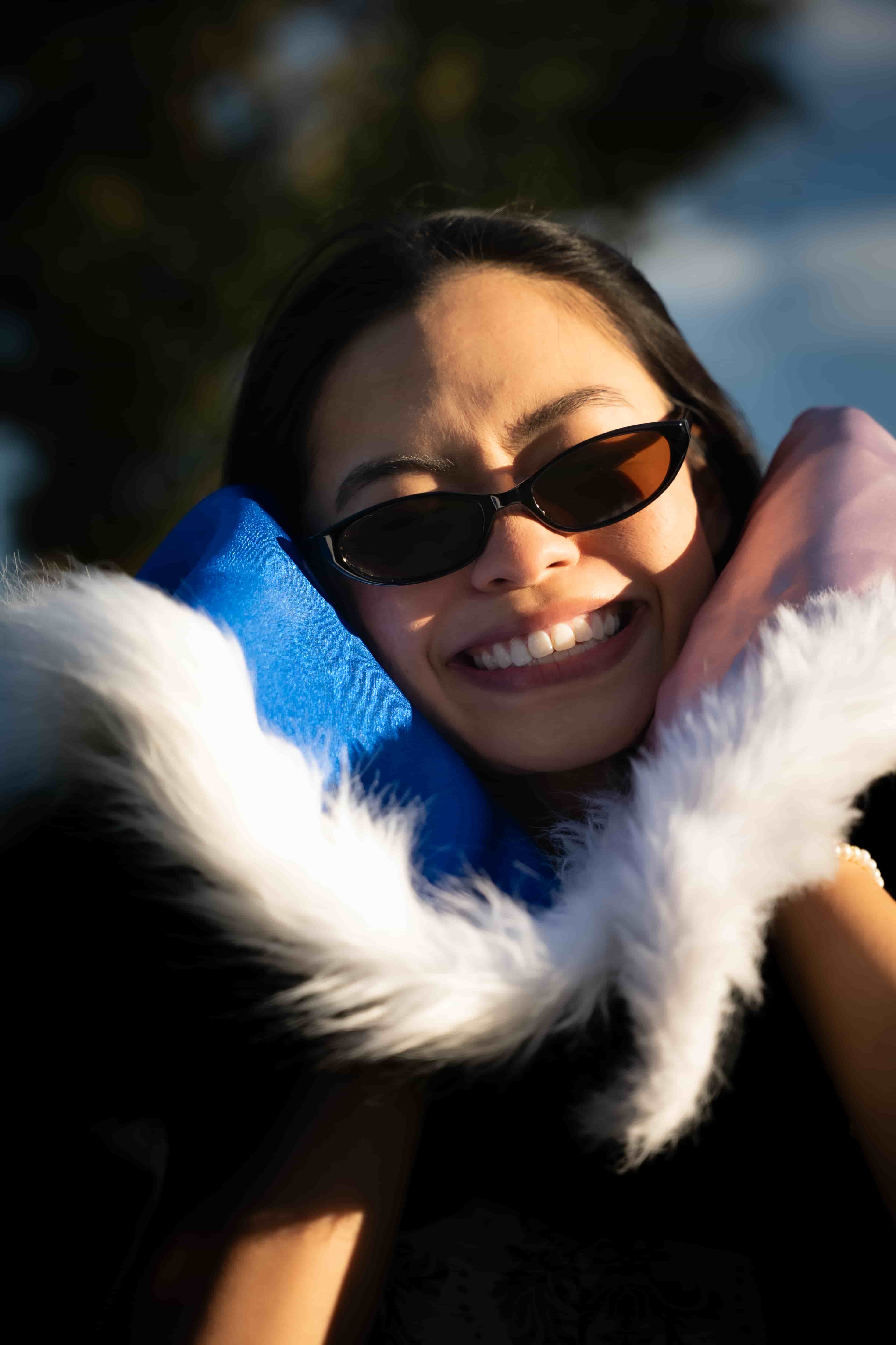 Ruby smiling in sunglasses with her blue and pink graduation hood pulled up around her face