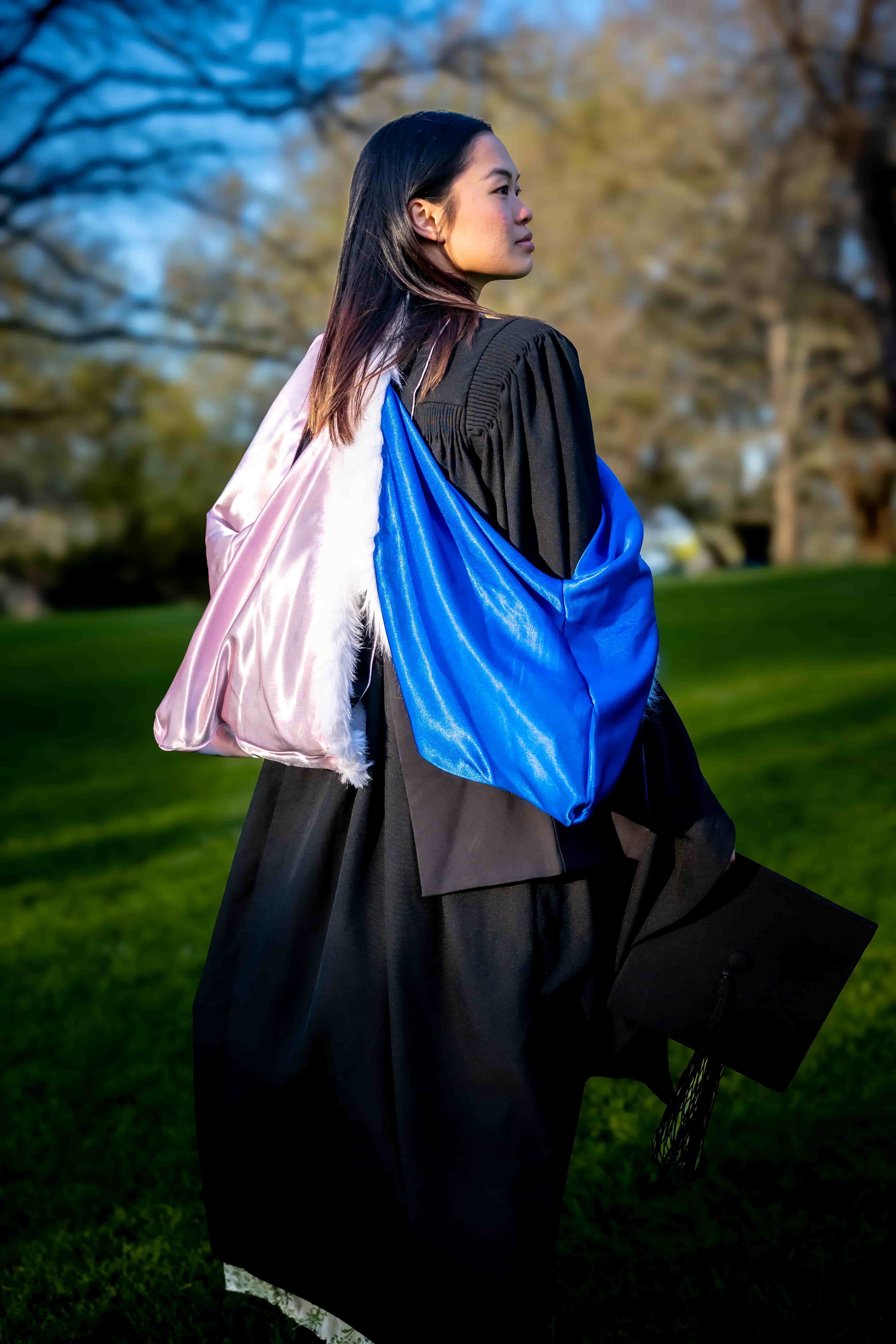 Ruby walking across the grass in her graduation gown, looking to the side in golden light