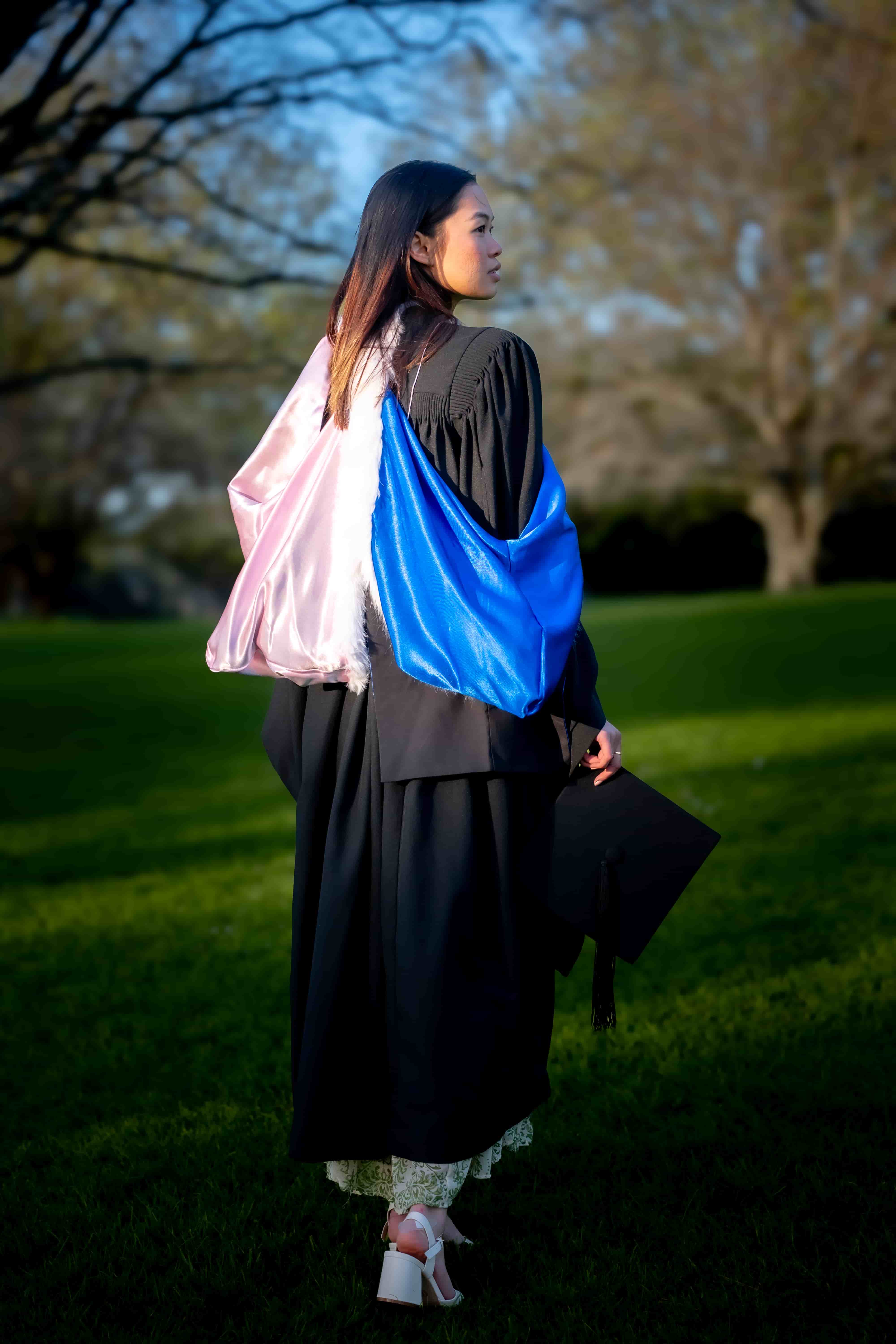 Ruby walking away through the Auckland Domain carrying her graduation cap at sunset