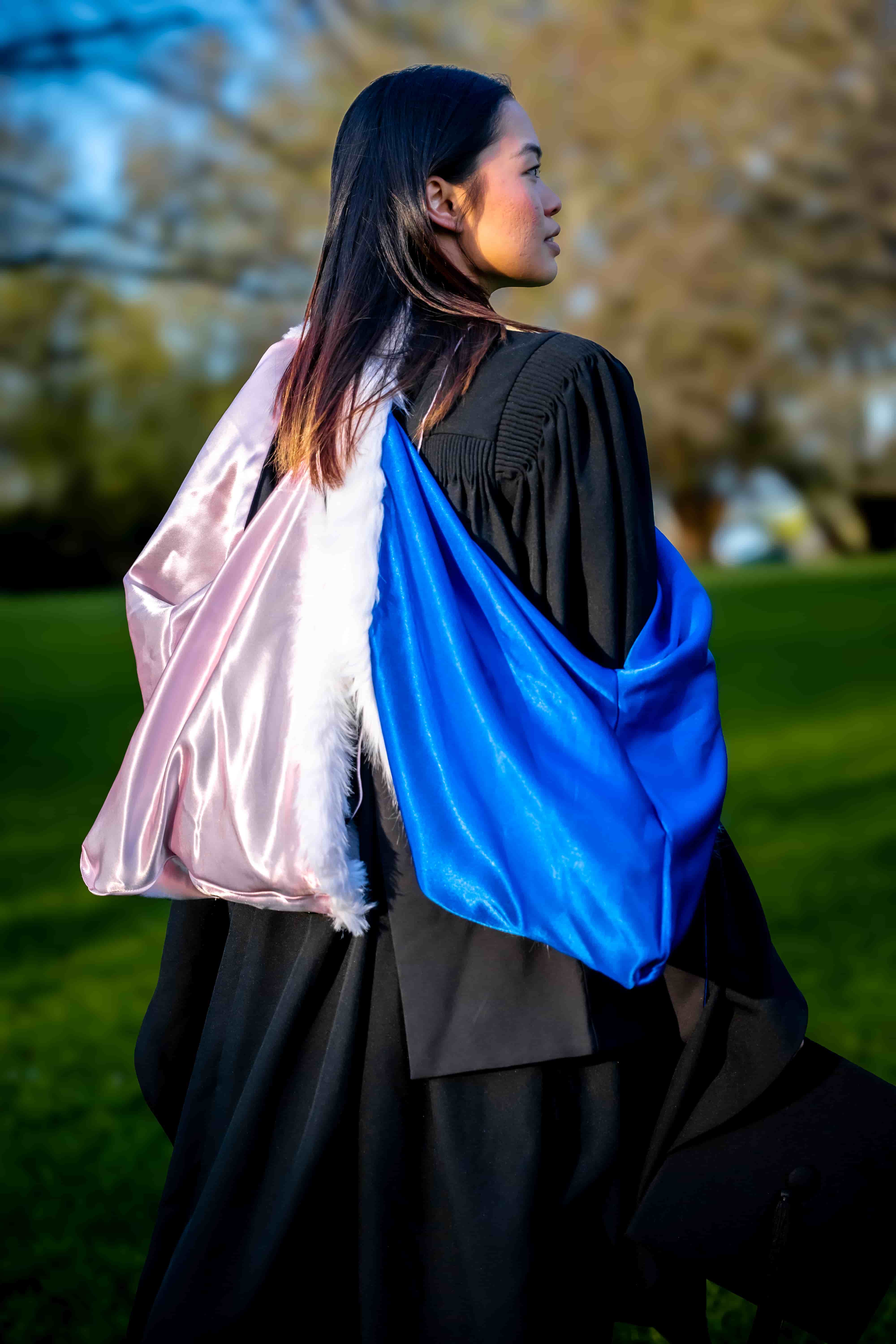 Back view of Ruby's graduation gown and blue and pink hood as she looks across the park