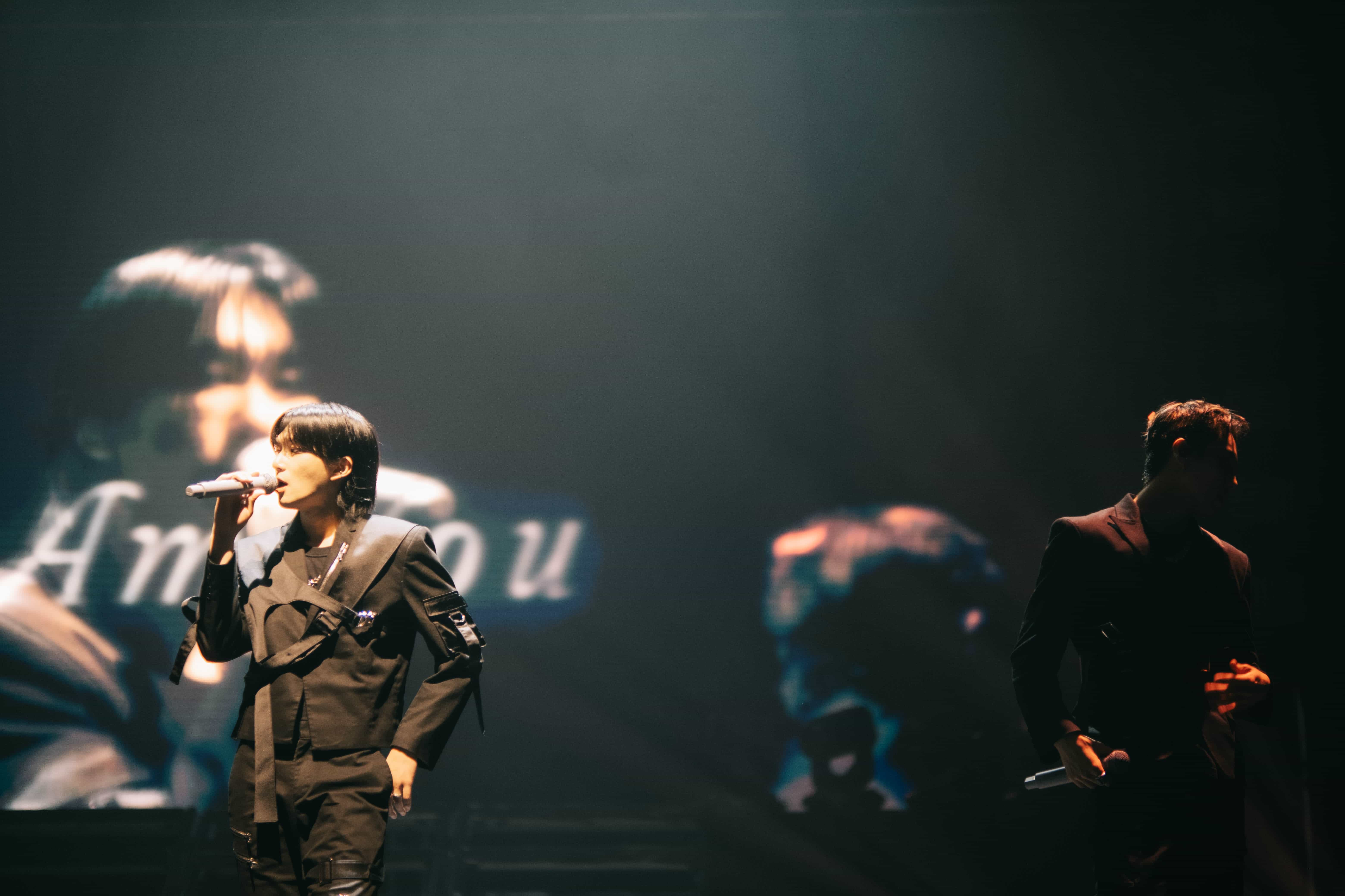 P1Harmony member singing in a black suit in front of the stage screen, Auckland concert