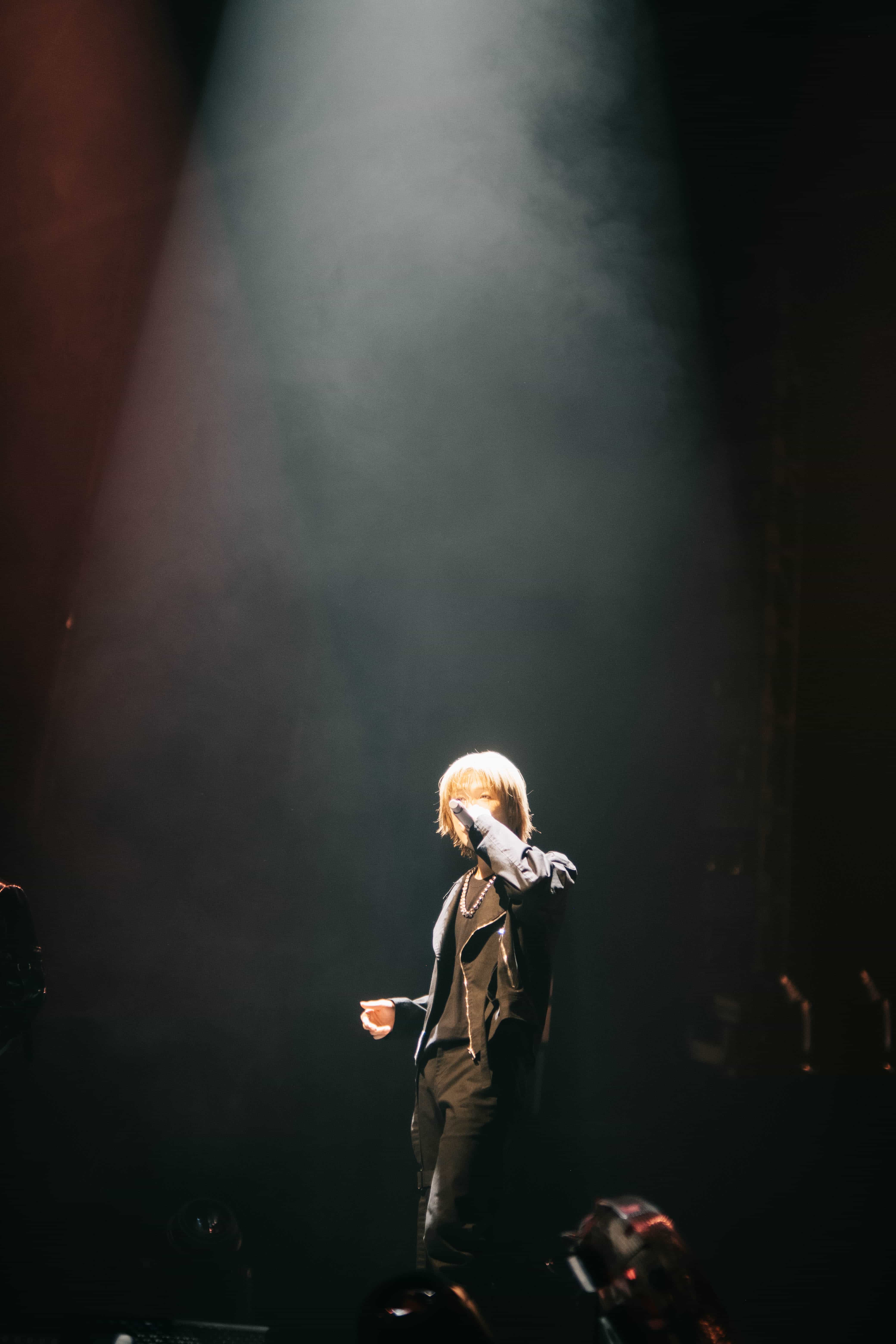 P1Harmony member in a dark jacket standing alone in a single shaft of hazy white light