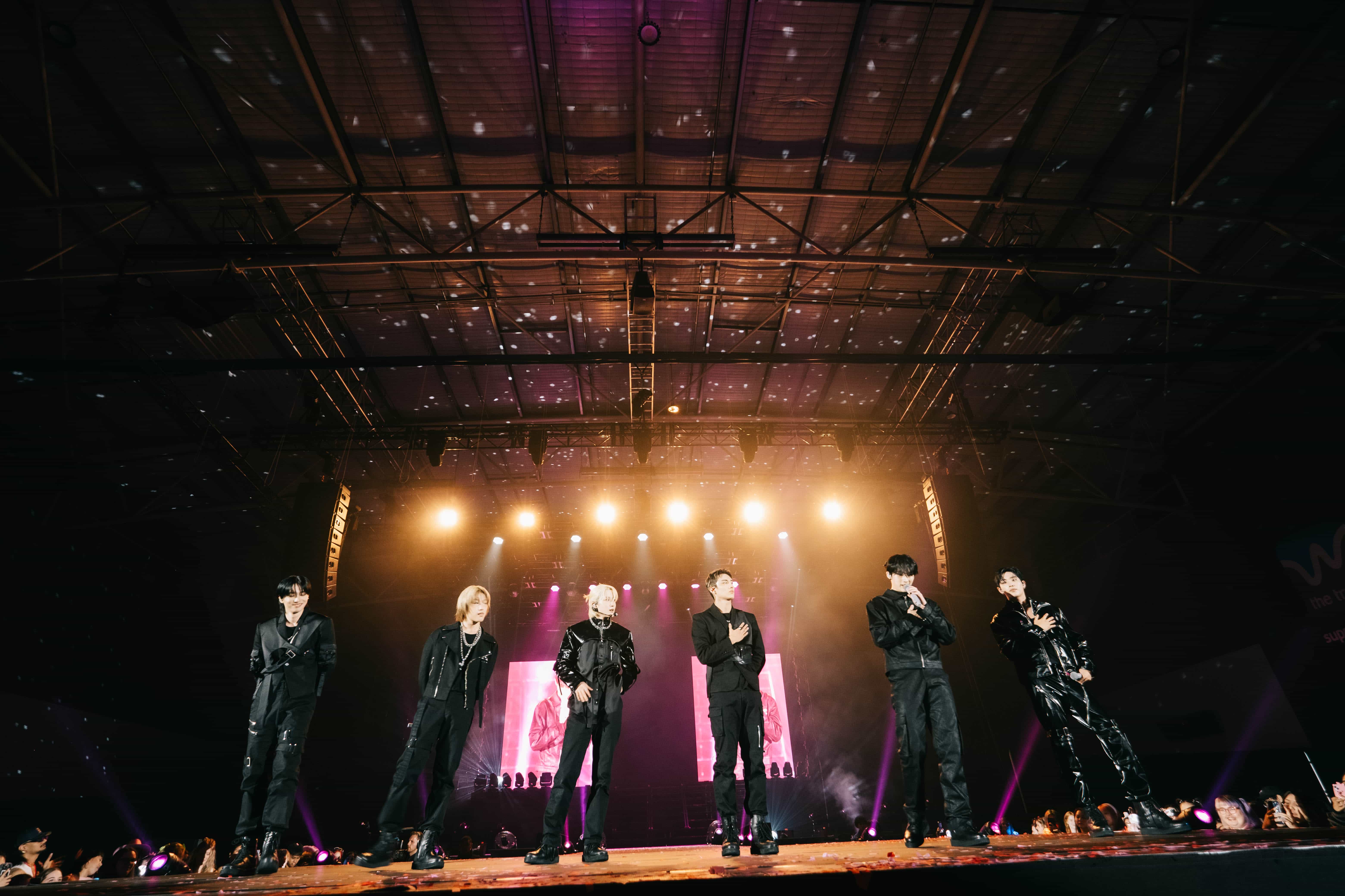 Six P1Harmony members standing in a row under a line of warm stage lights, UTOP1A tour Auckland