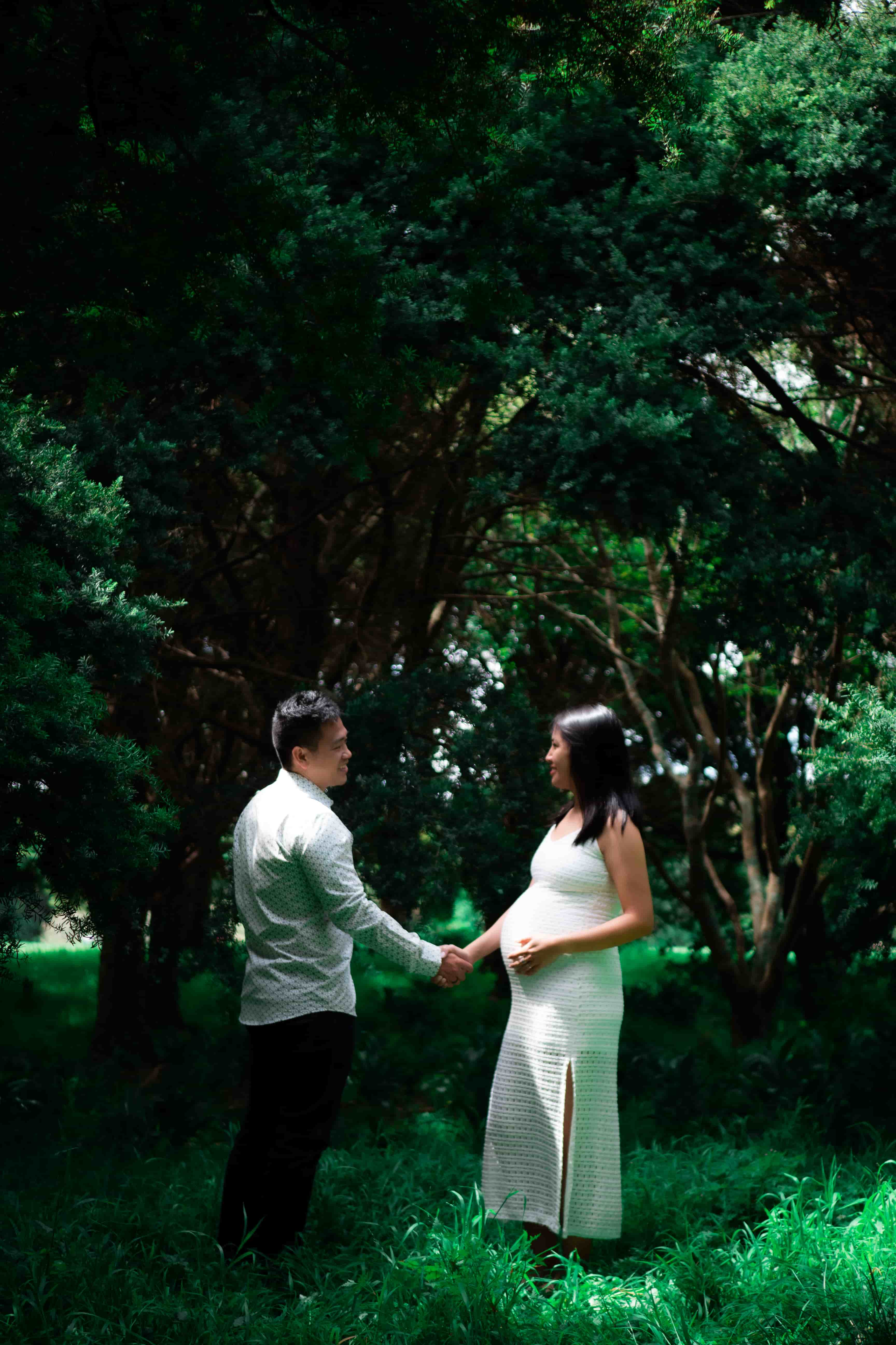 Lucas and Elisa holding hands in a green clearing under tall trees