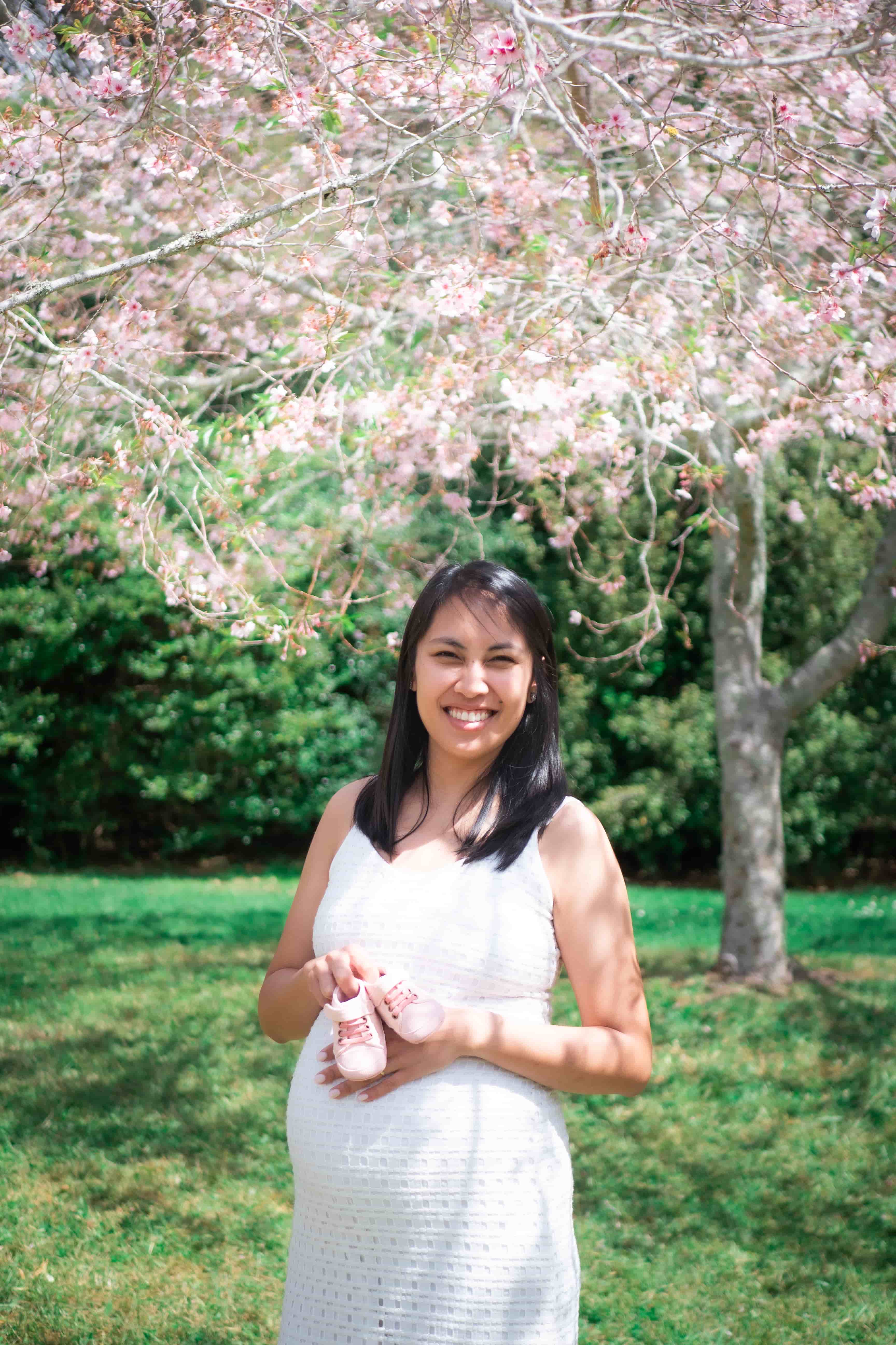 Elisa holding tiny pink baby shoes beneath a cherry blossom tree