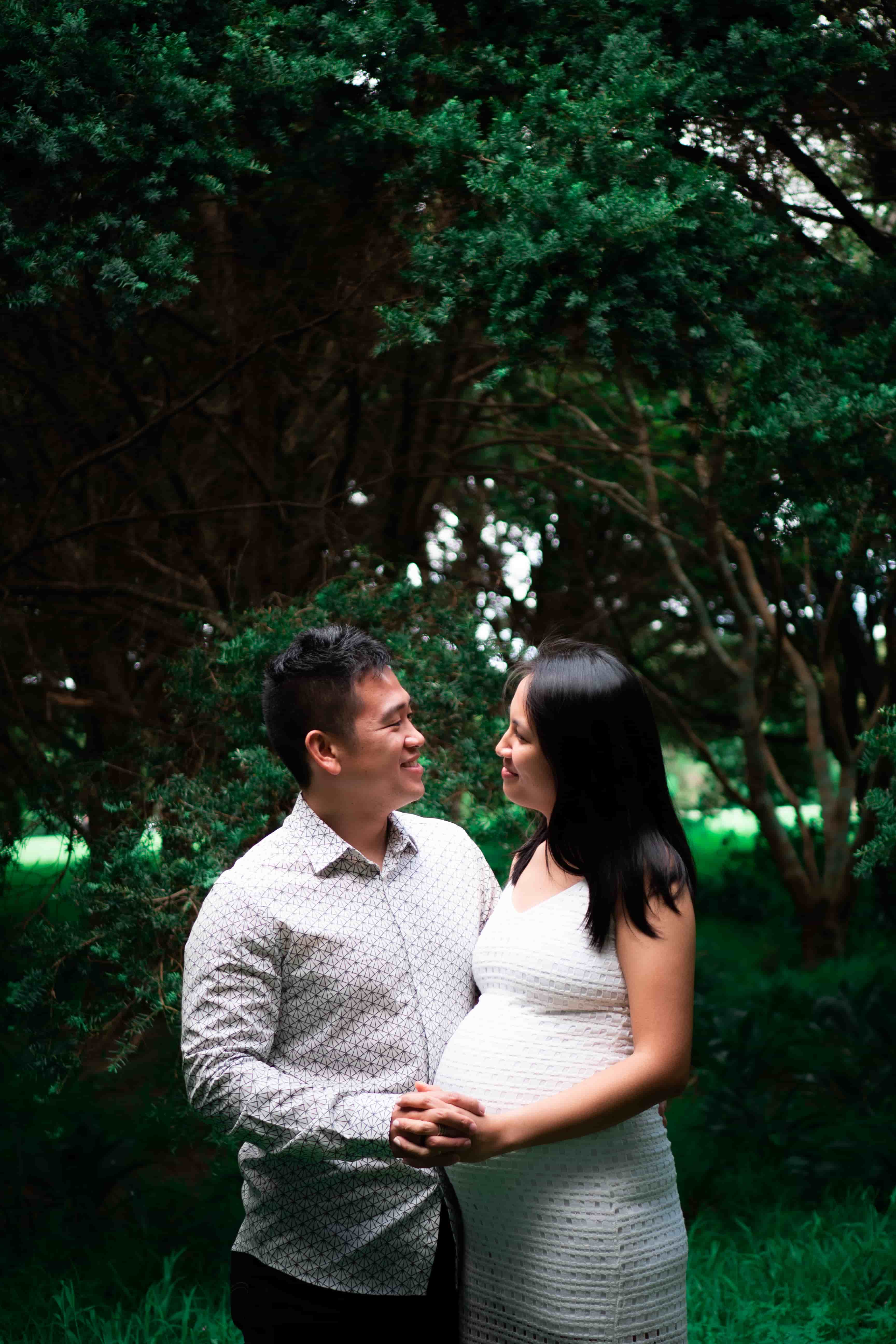 Lucas and Elisa face each other under tall trees, his hand on her bump