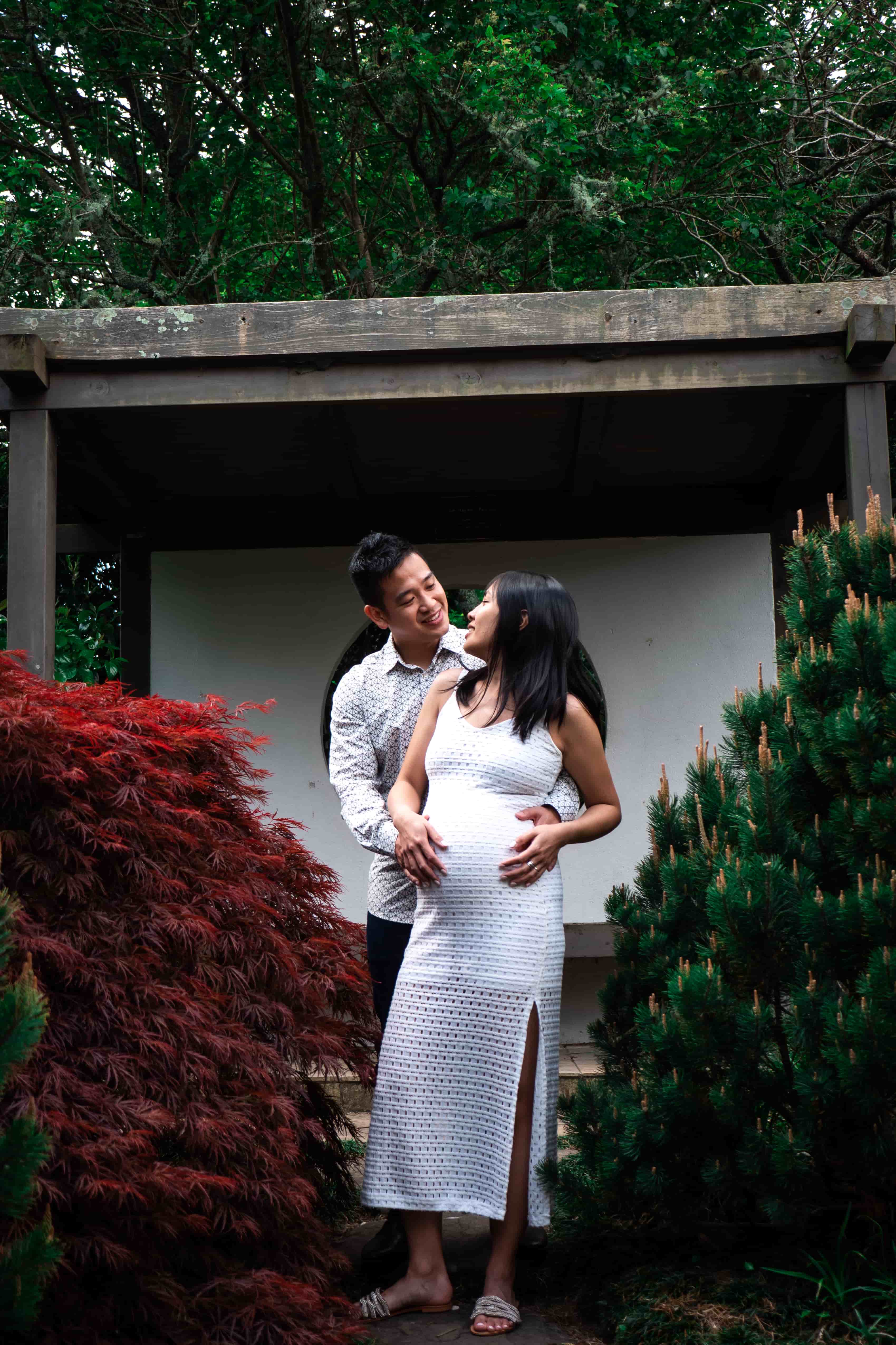 Lucas holding Elisa from behind beside a red maple and a white pavilion