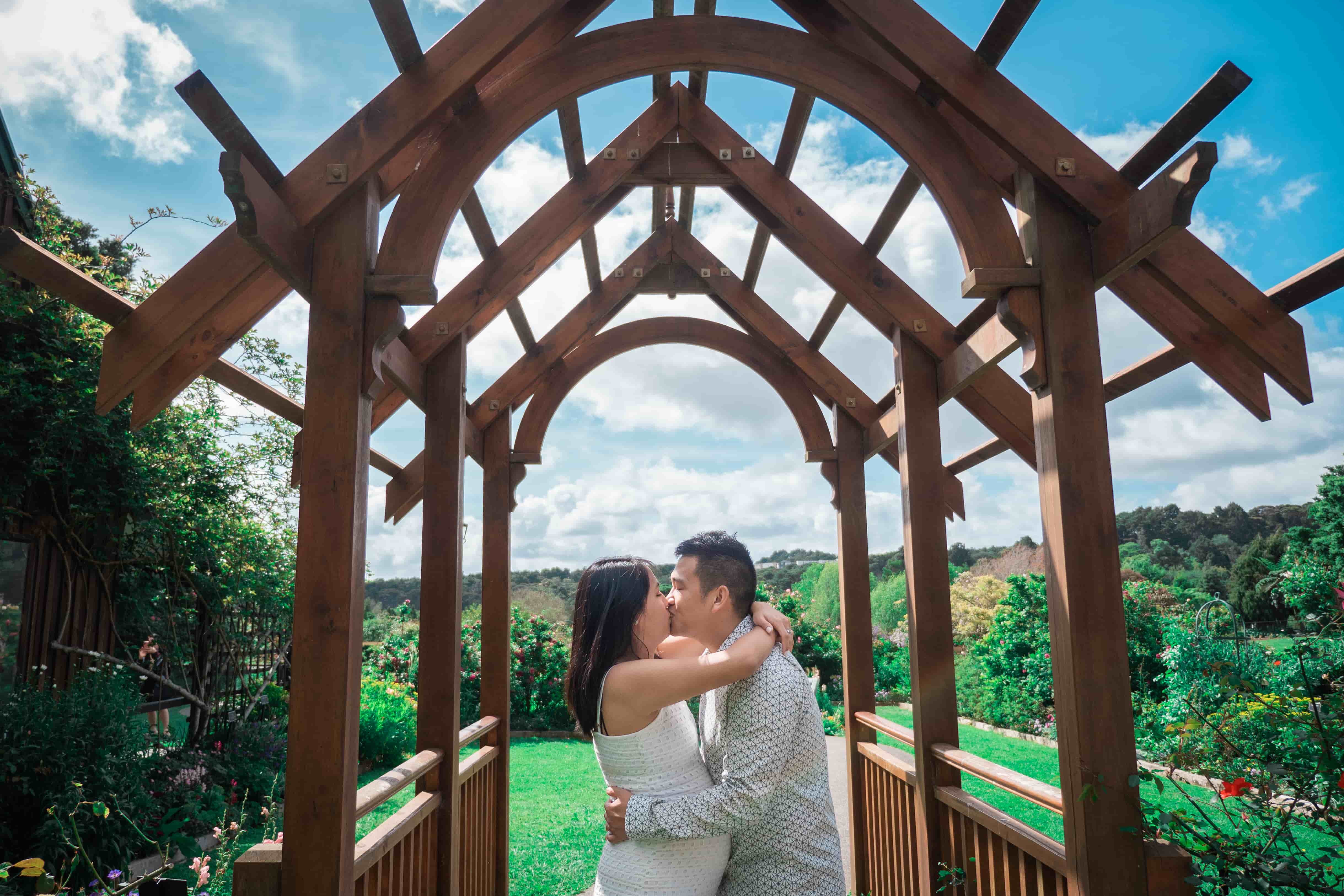 Lucas and Elisa kissing under a wooden pergola with green hills behind