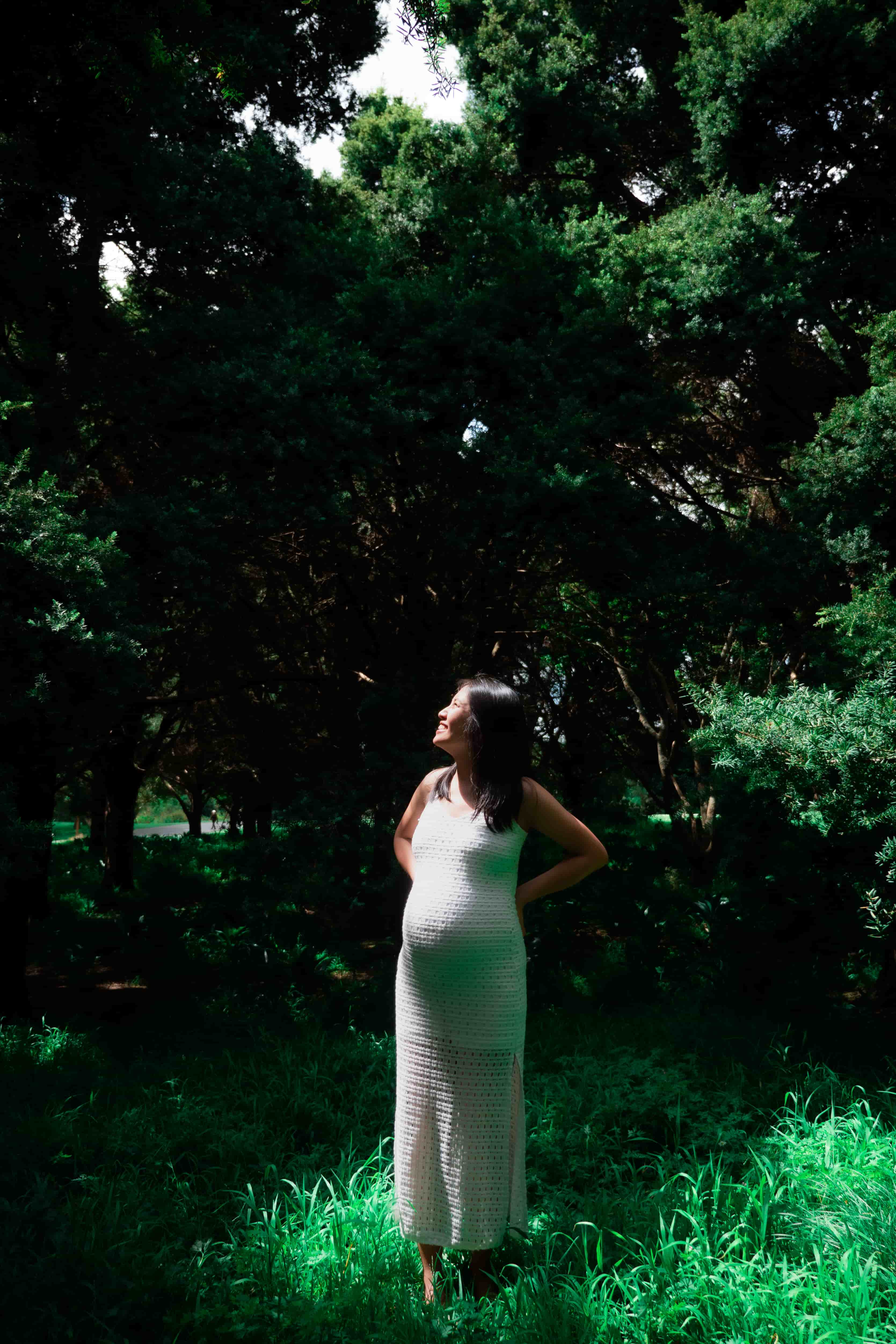 Elisa standing in long grass, looking back over her shoulder in a sunlit grove