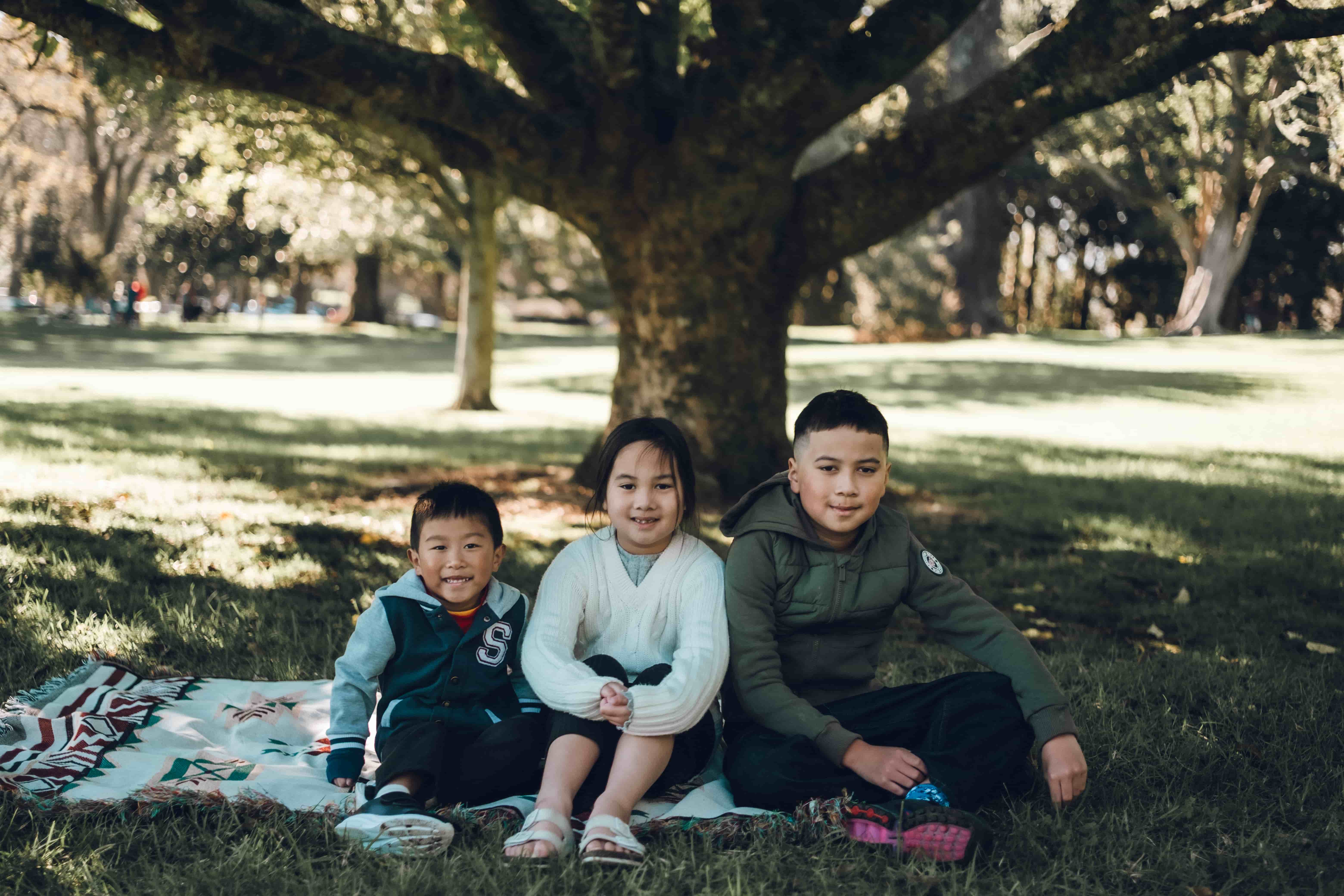 Three children smiling on a blanket on the grass