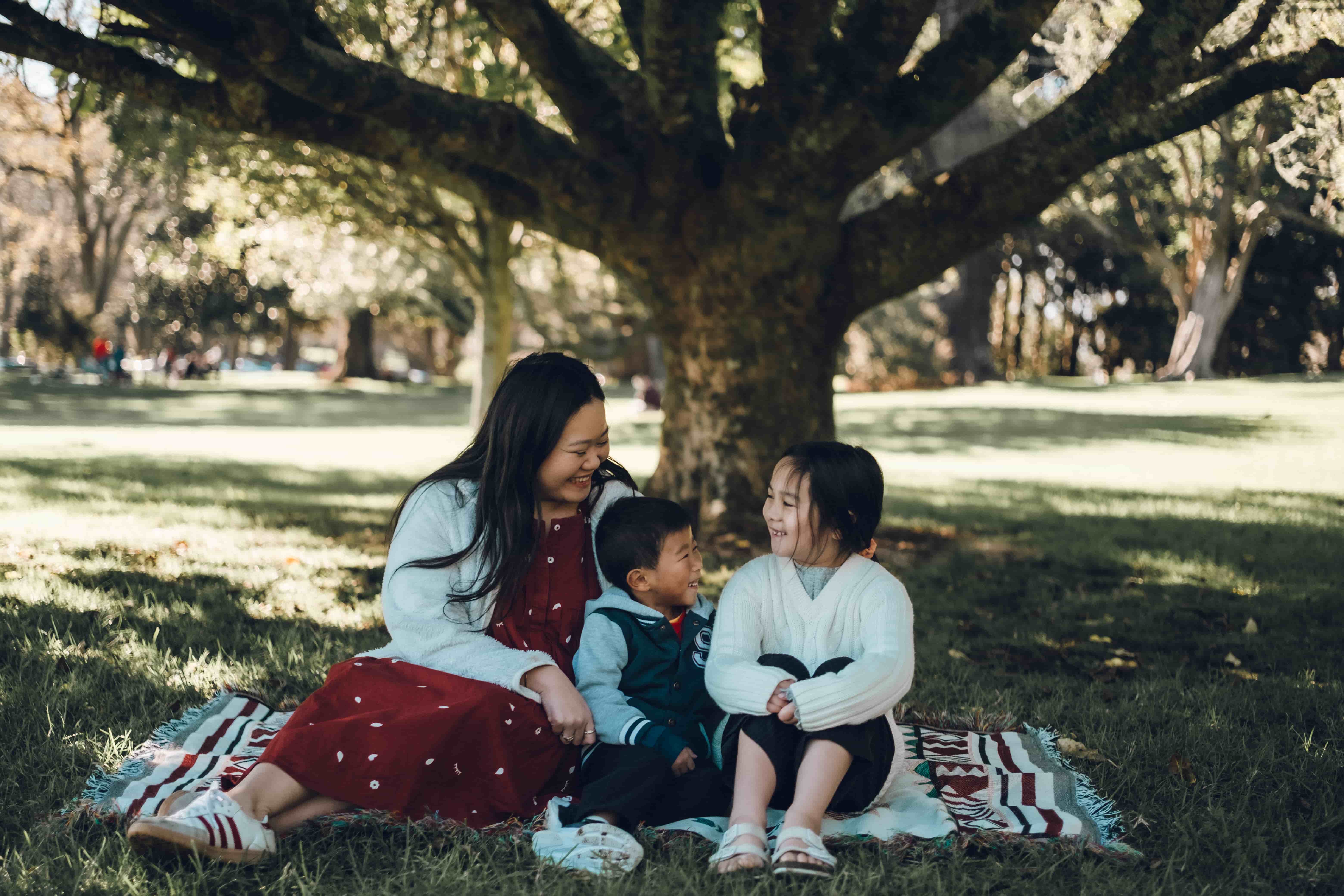 Mother and two children laughing on a picnic blanket on the lawn