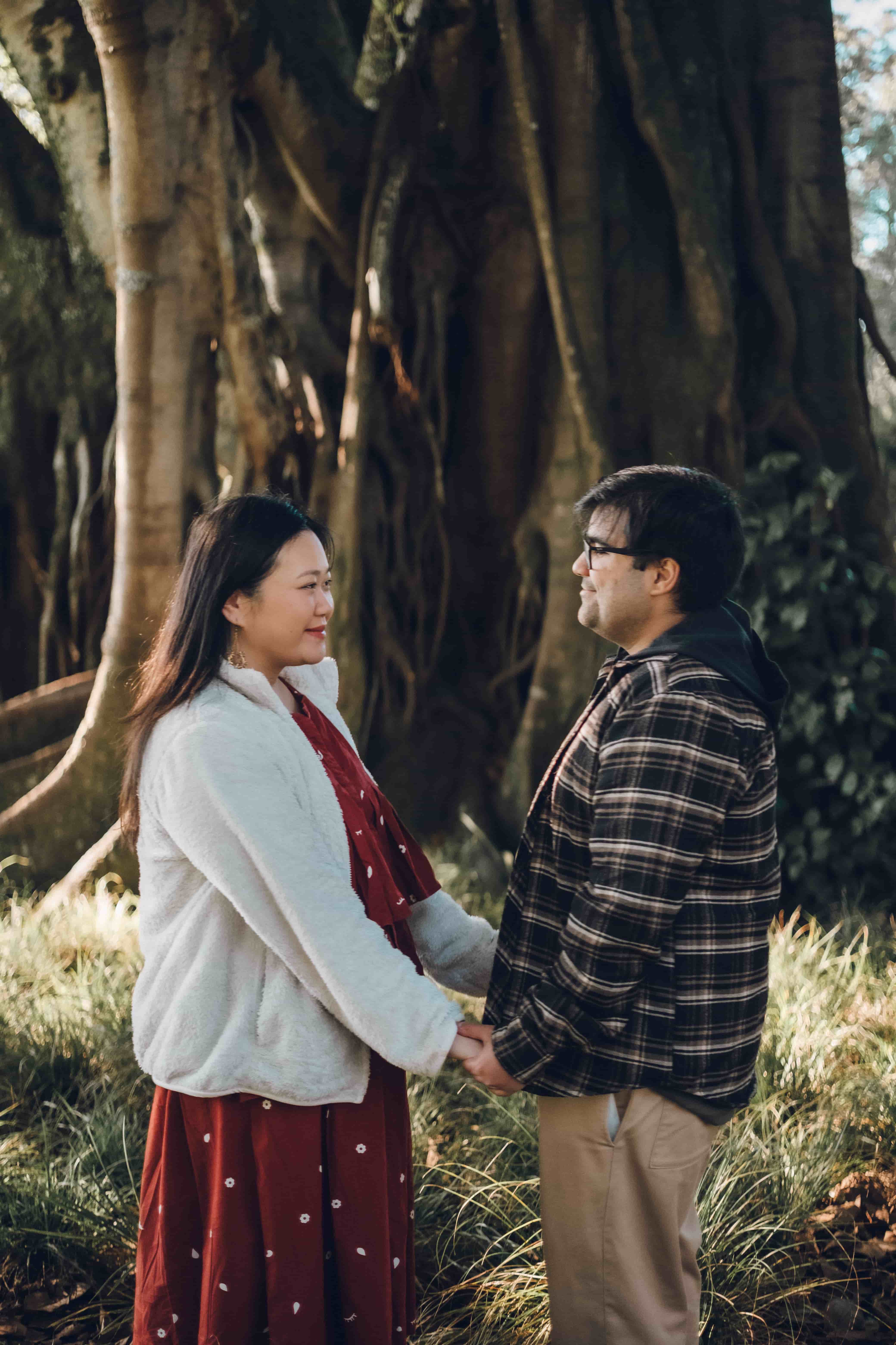Couple facing each other and holding hands under a big tree
