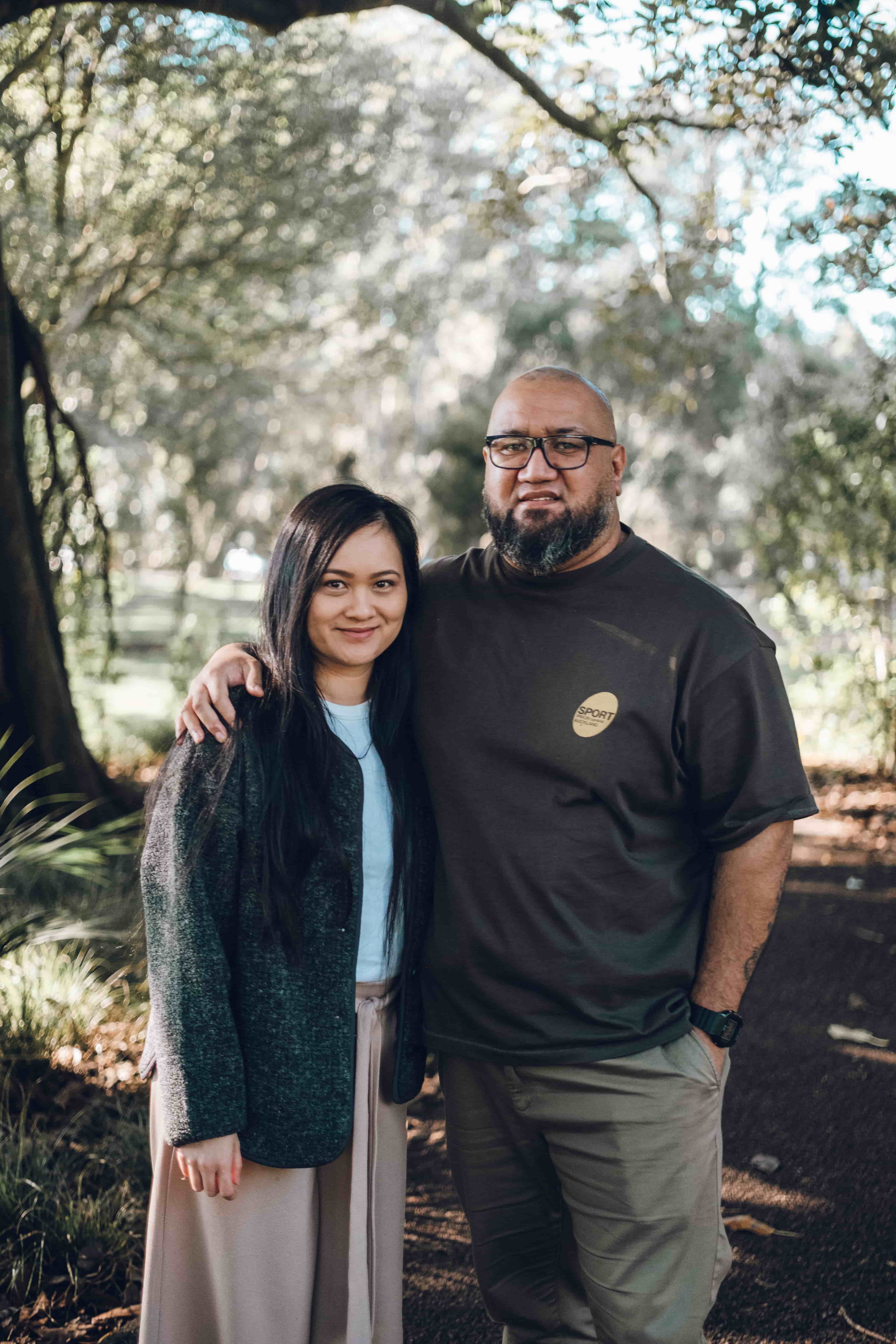 Couple standing close on a park path under arching branches
