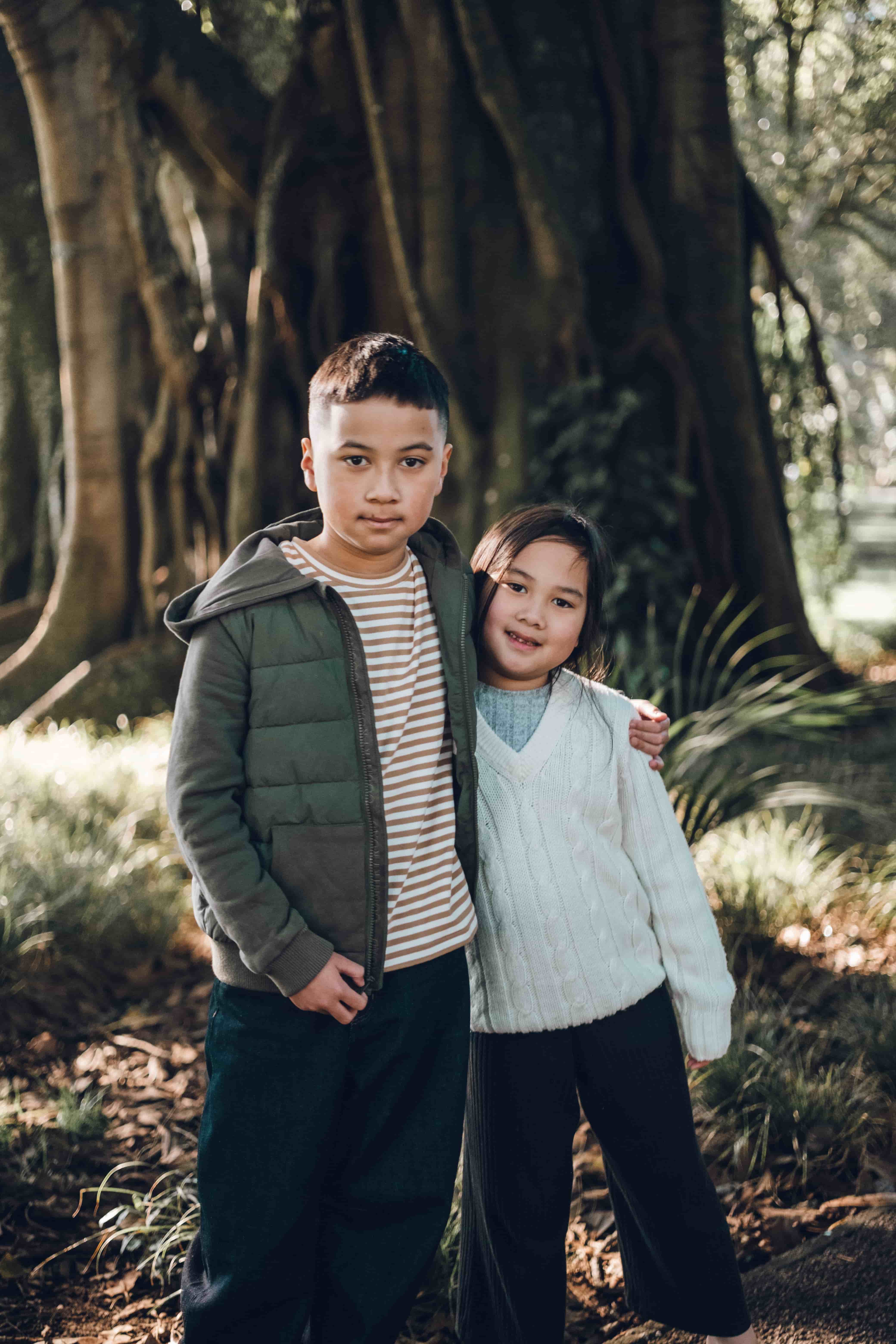Brother and sister side by side in front of a sprawling tree