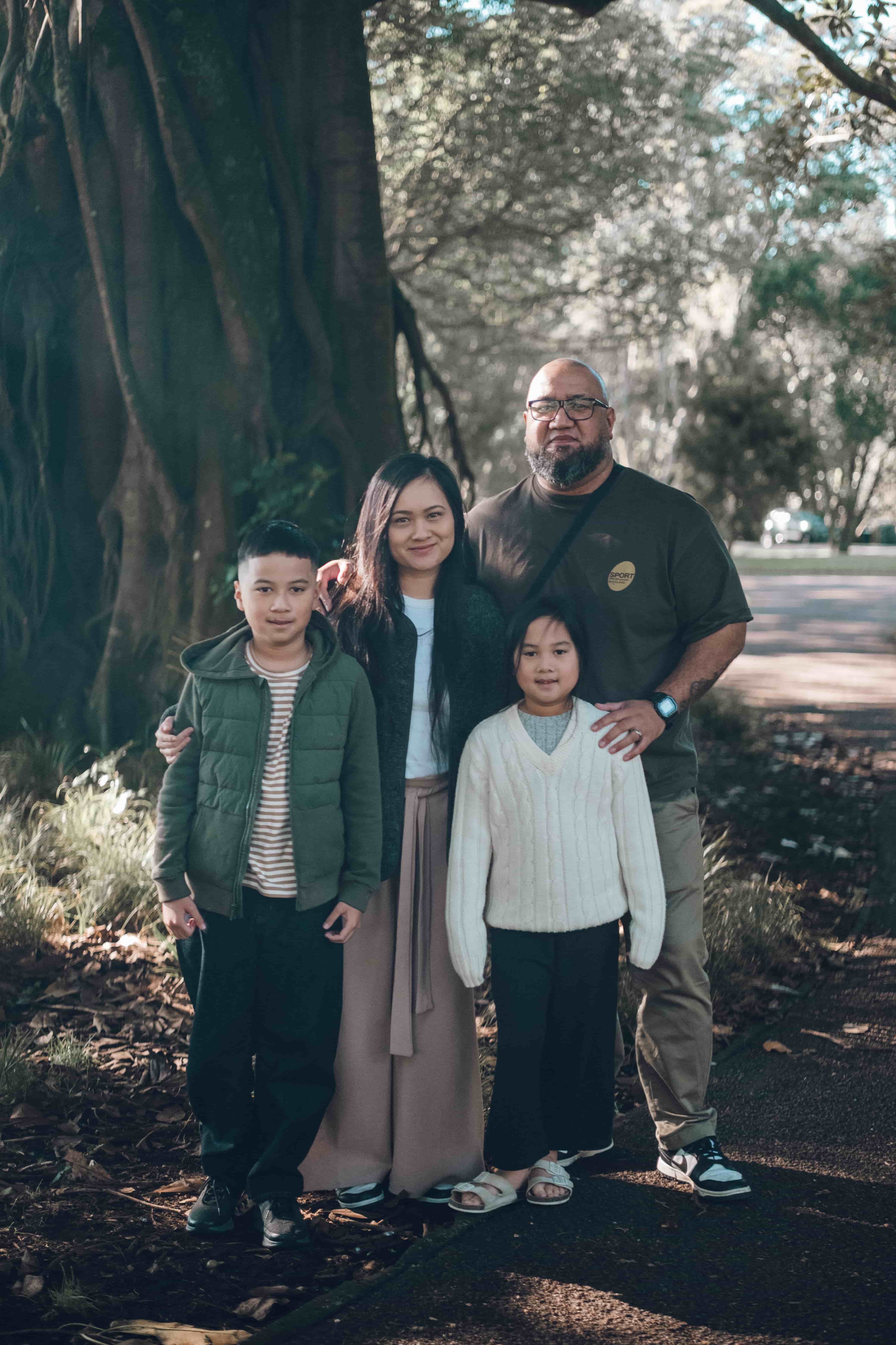 Family of four standing on a park path under large old trees