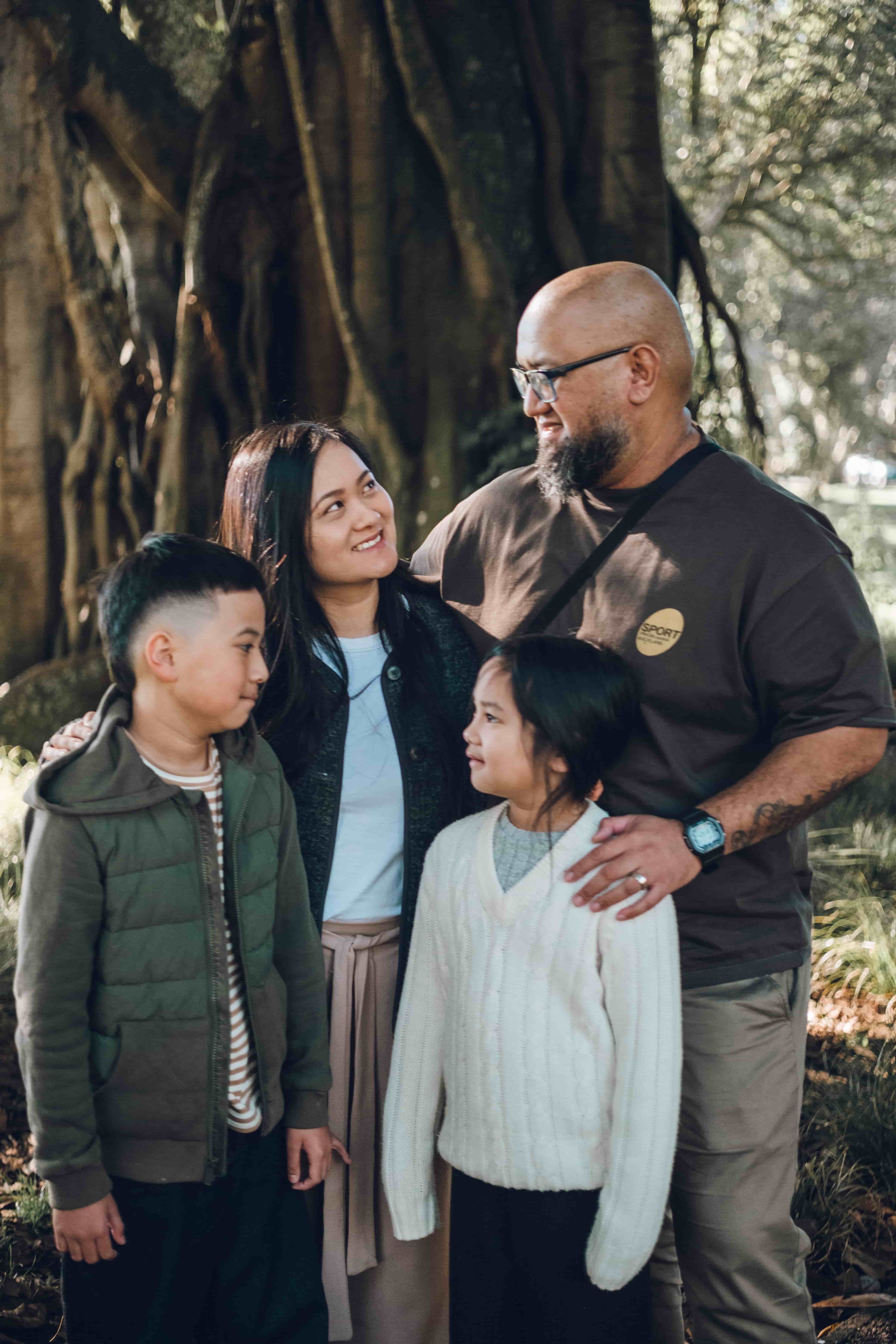 Parents and two children smiling together in front of a tree trunk
