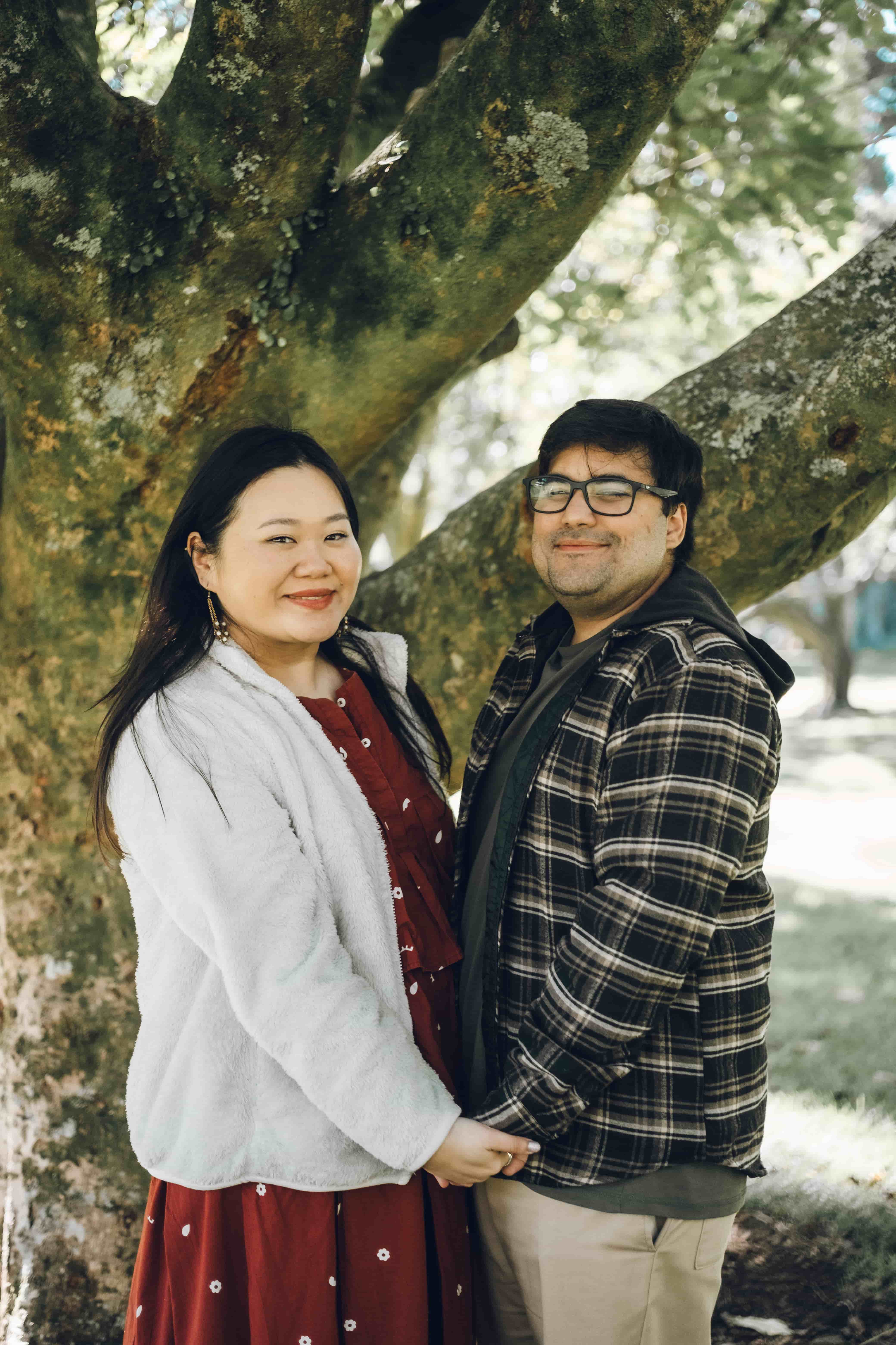 Couple holding hands in front of a mossy tree trunk