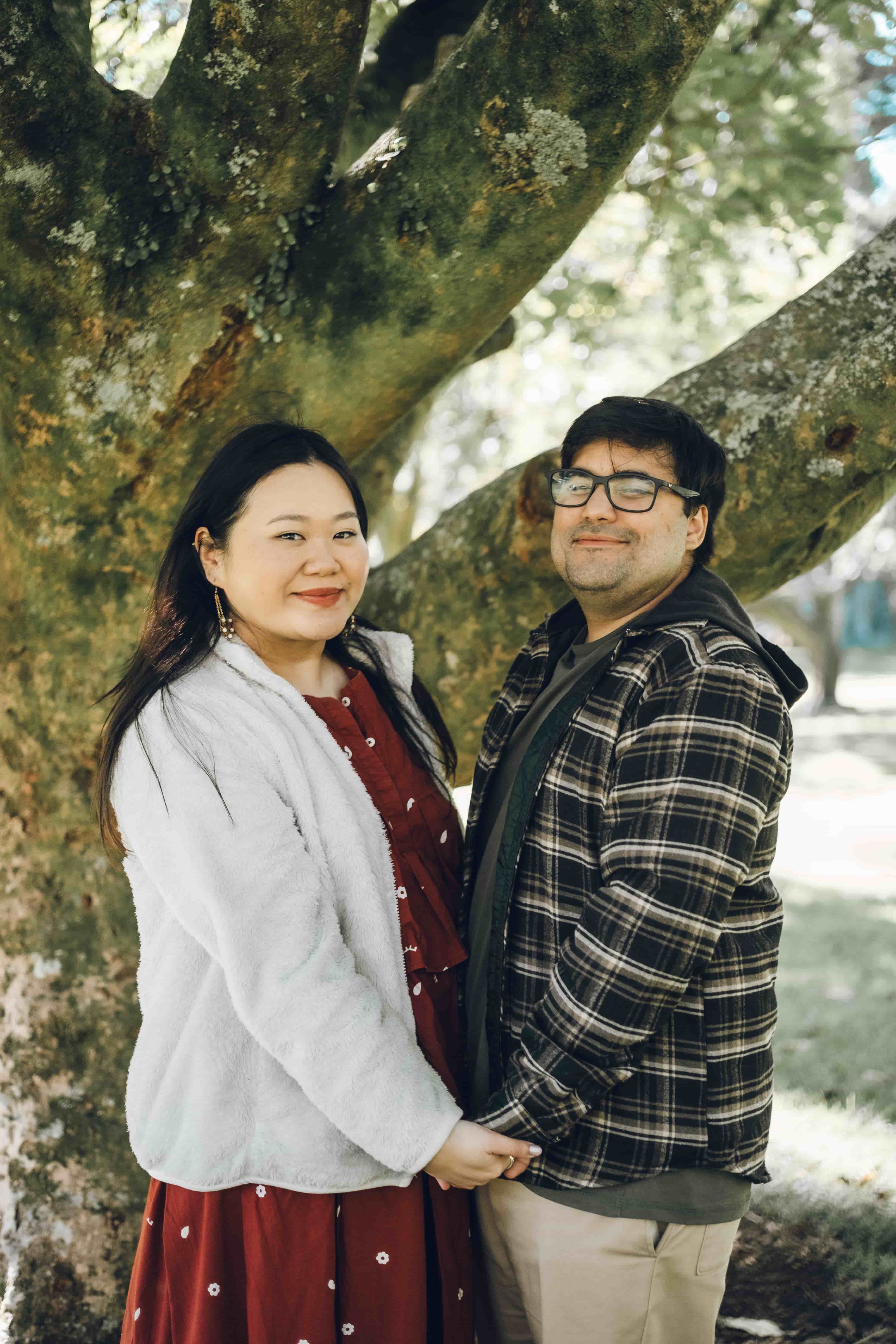 Couple smiling side by side against a mossy tree