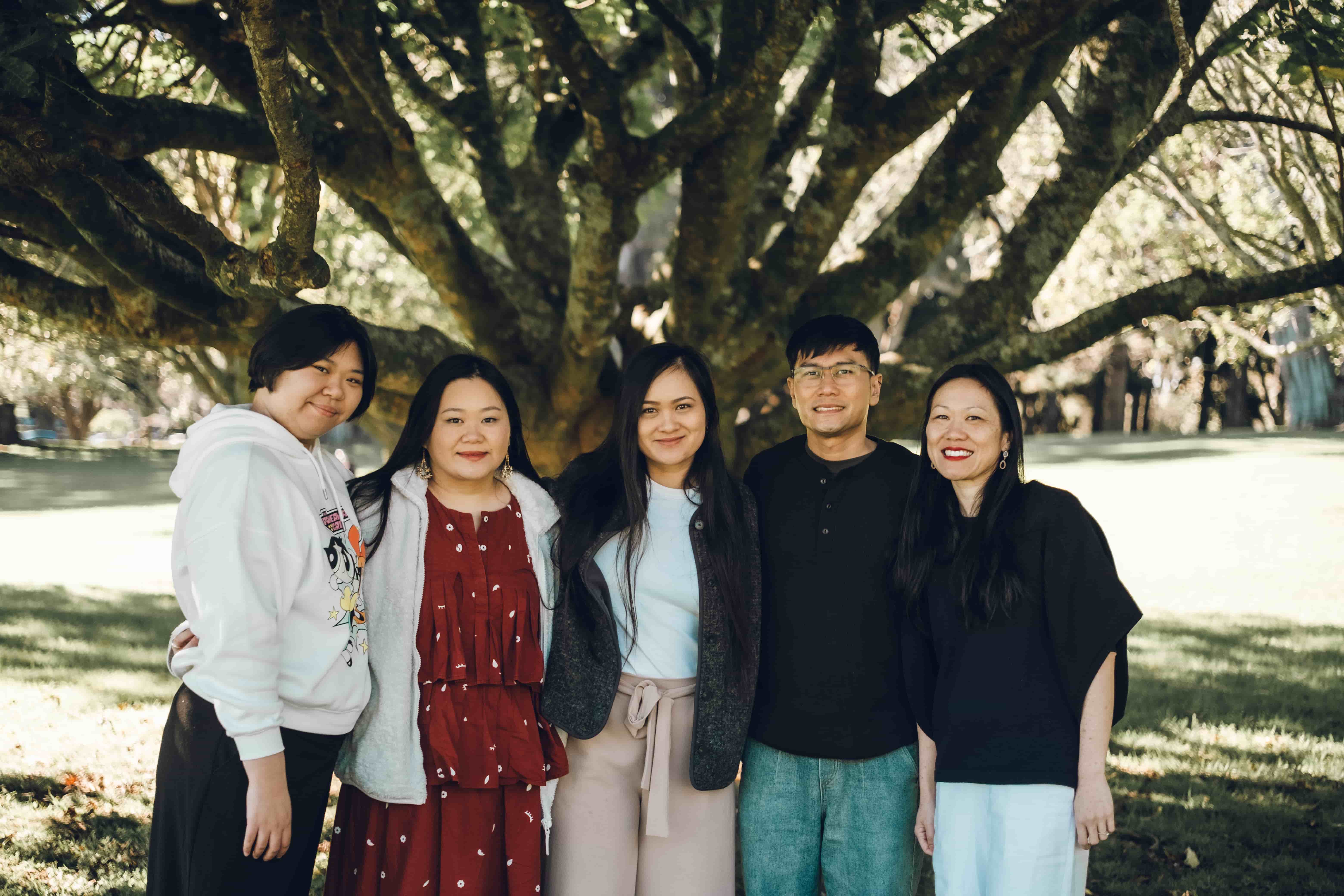 Five family members standing arm in arm under a big tree