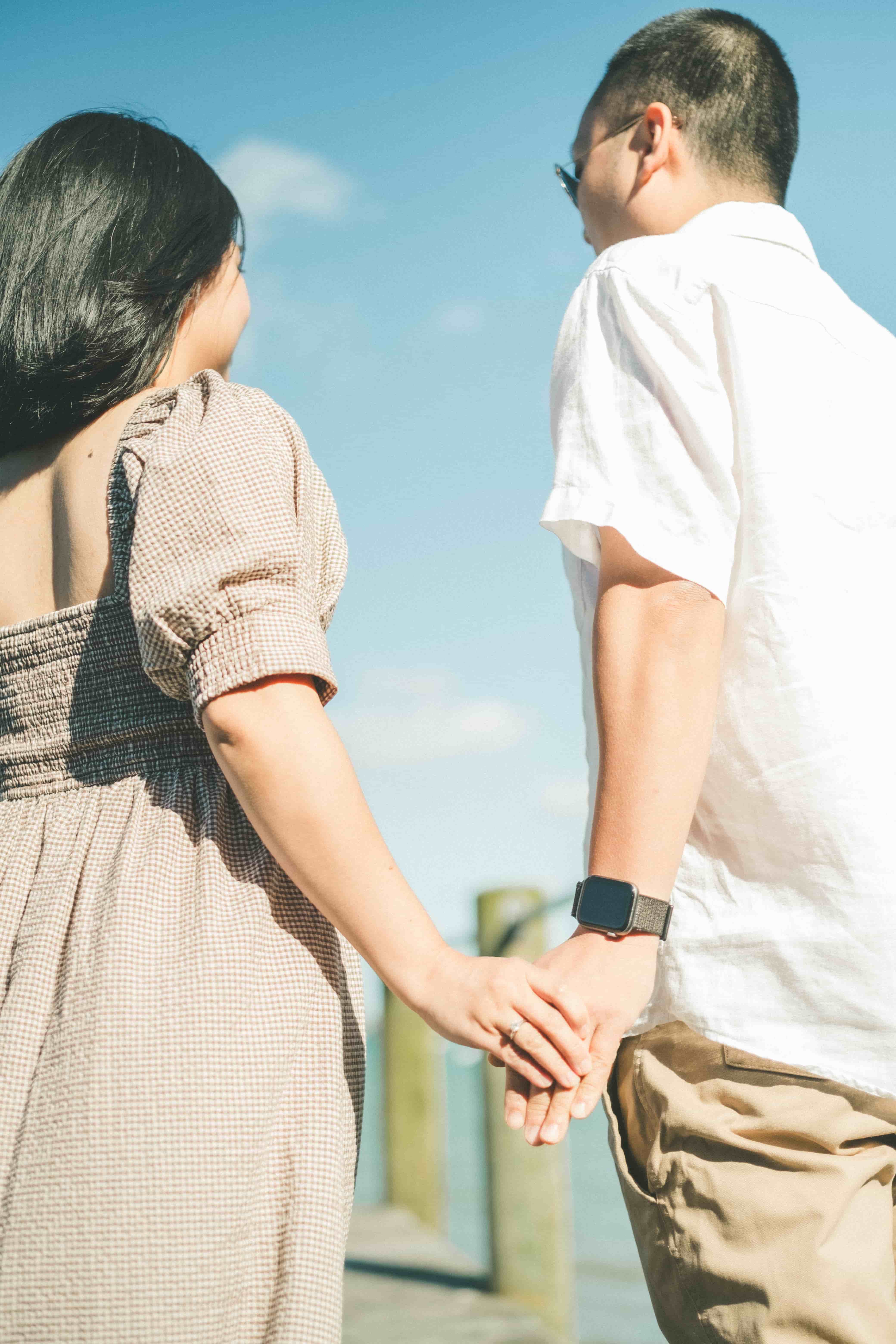 Couple holding hands on a wharf under a blue sky, seen from behind