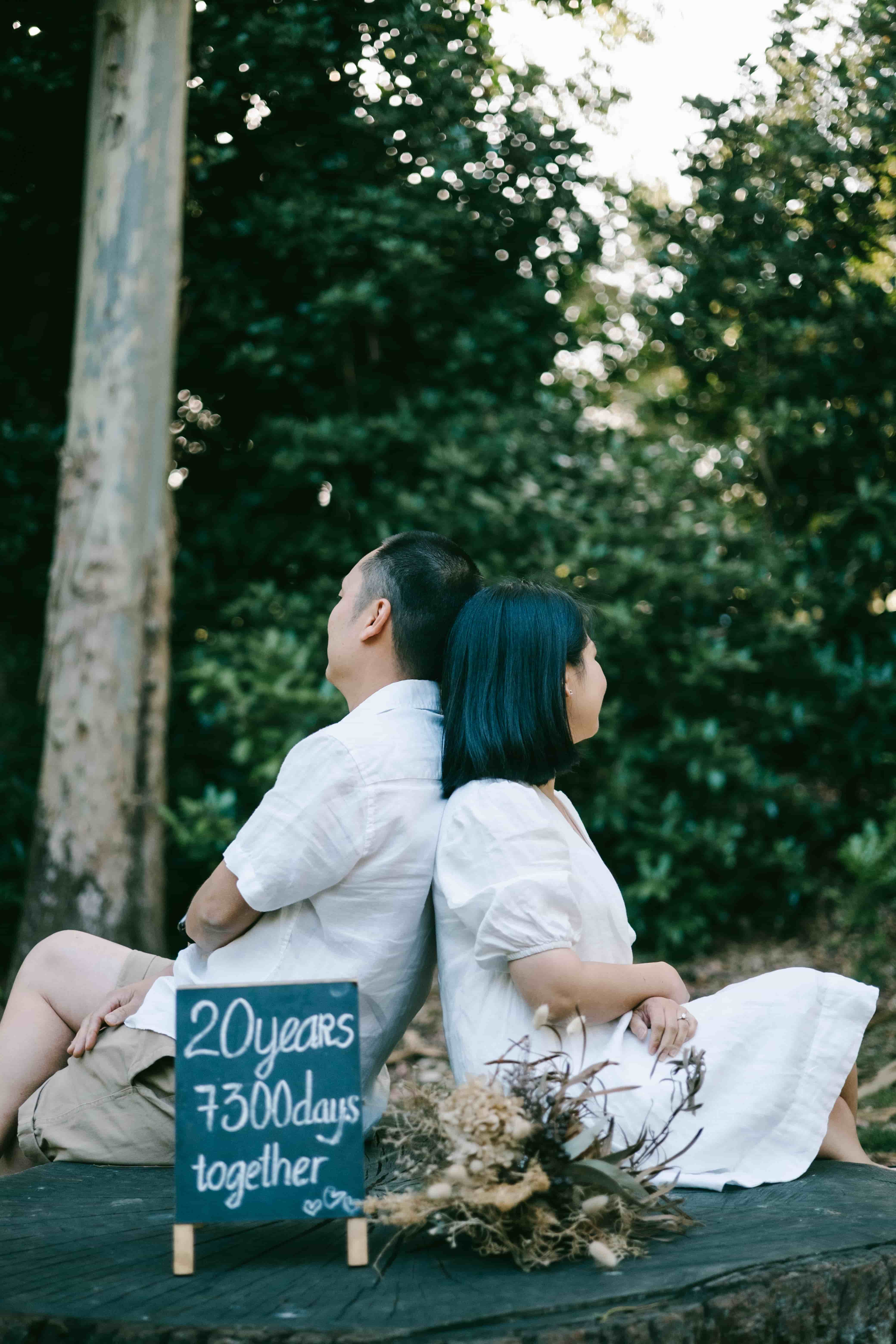 Couple sitting back to back on a tree stump beside the chalkboard