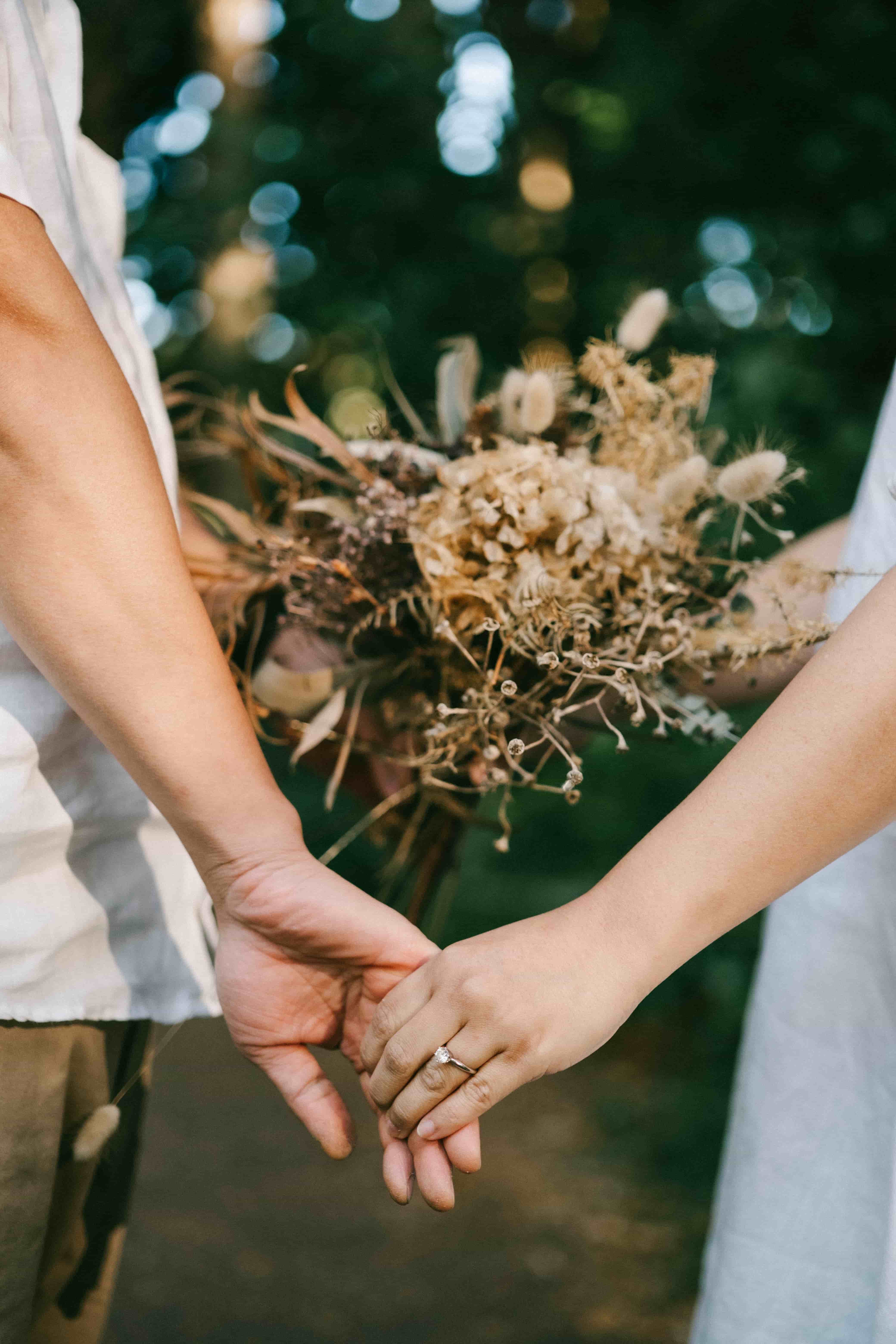 Close-up of the couple holding hands beside dried flowers