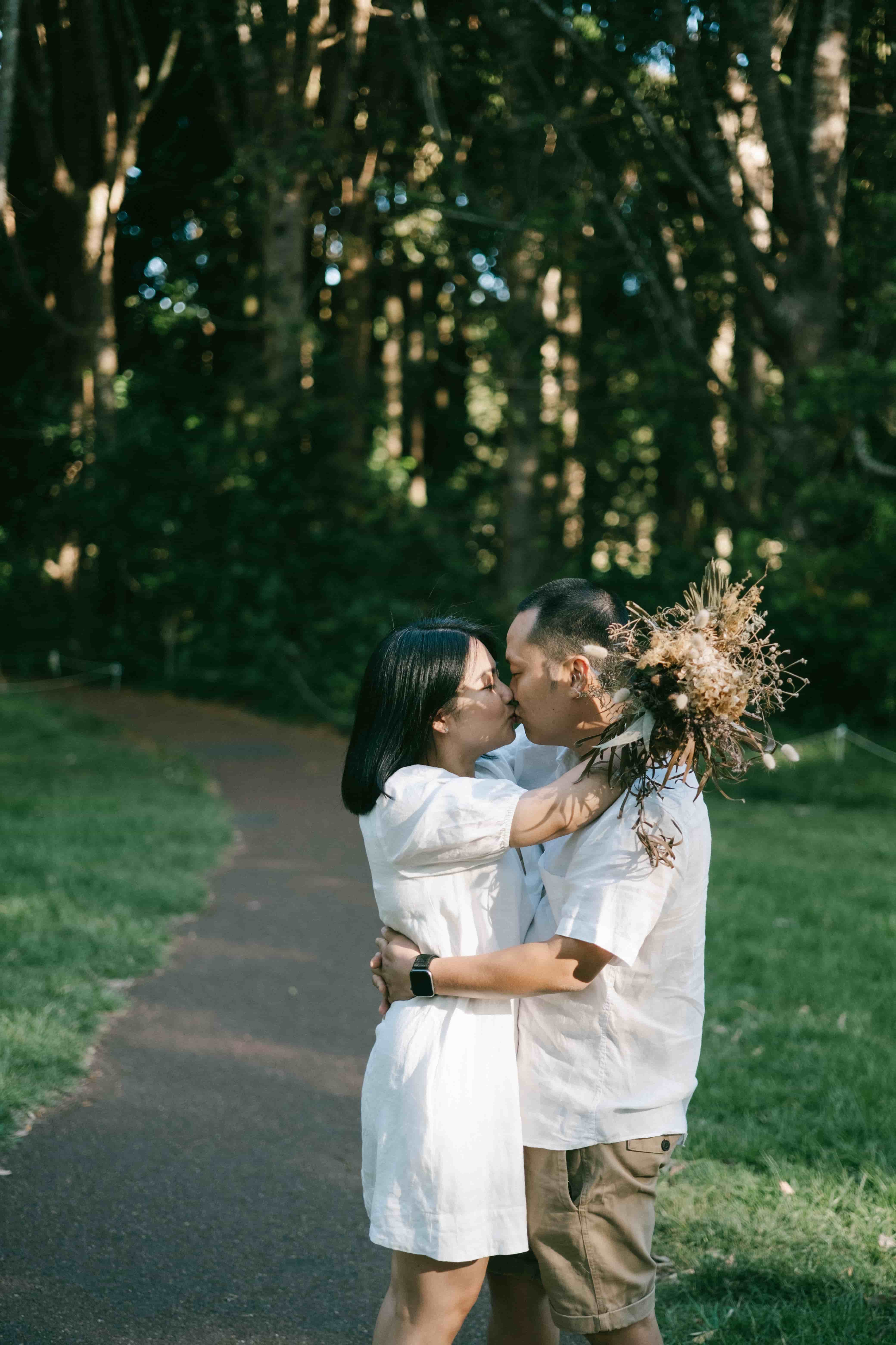Couple kissing on a winding path, bouquet in hand