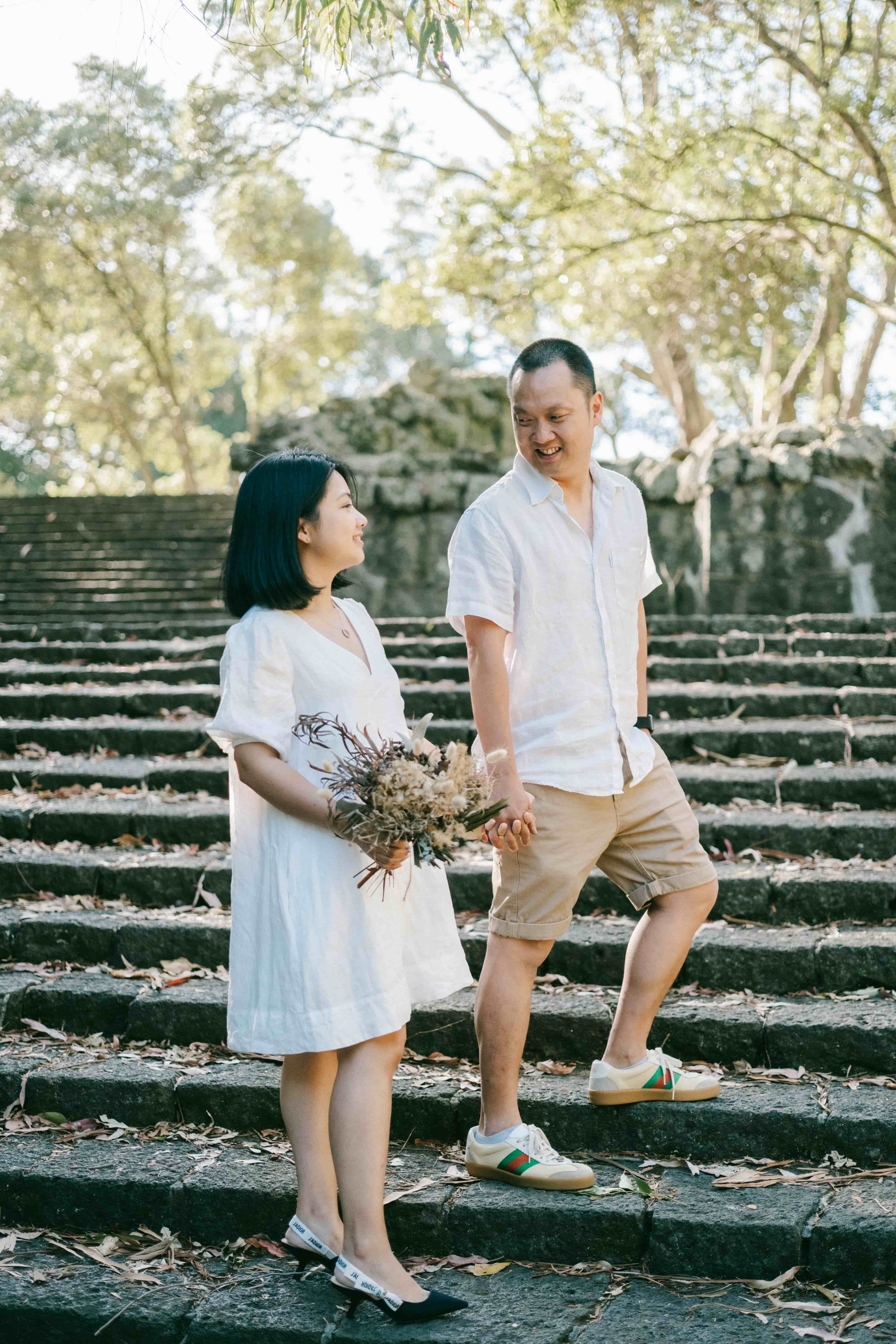Couple standing on wide stone steps under tall trees