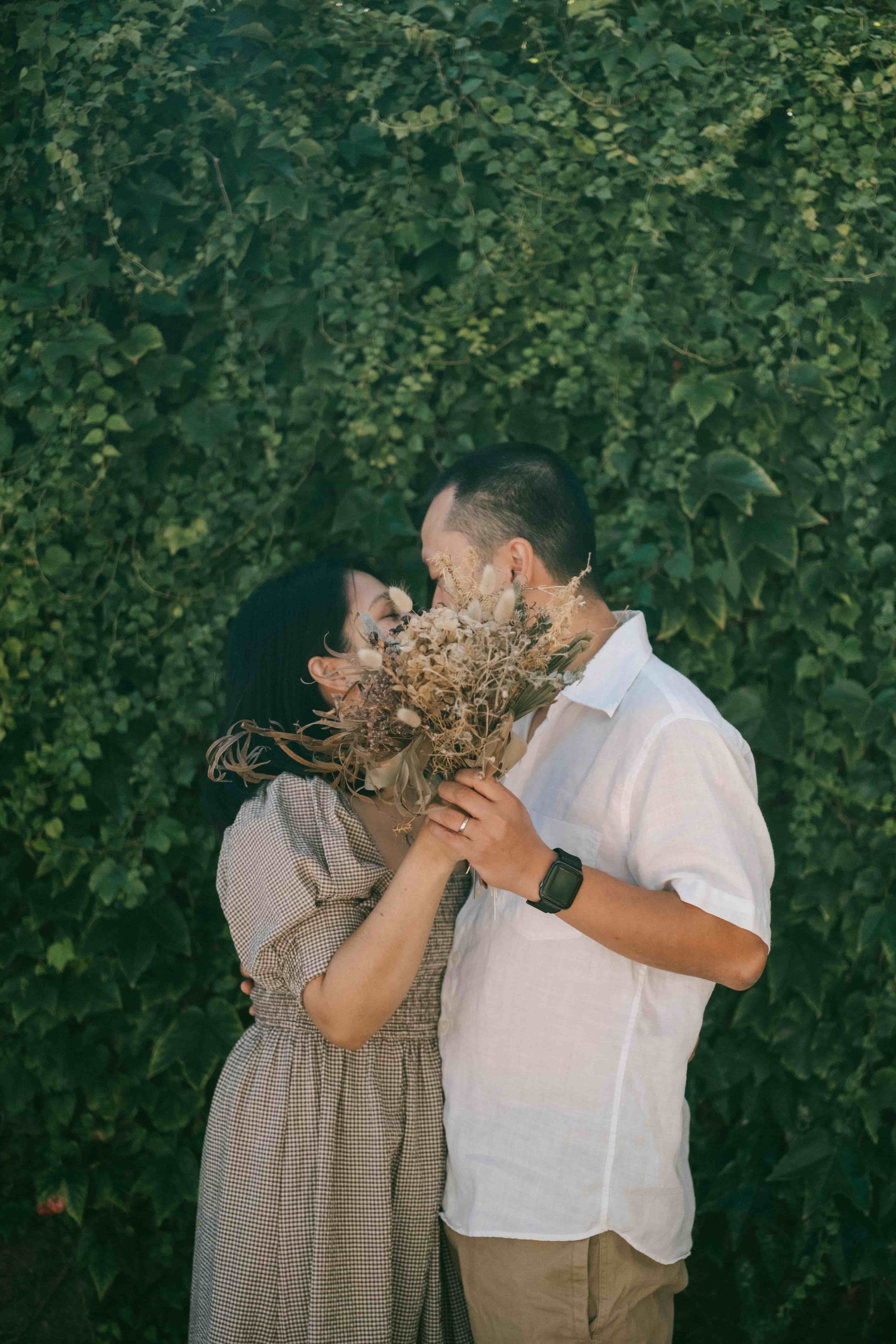 Couple sharing a kiss behind a dried flower bouquet