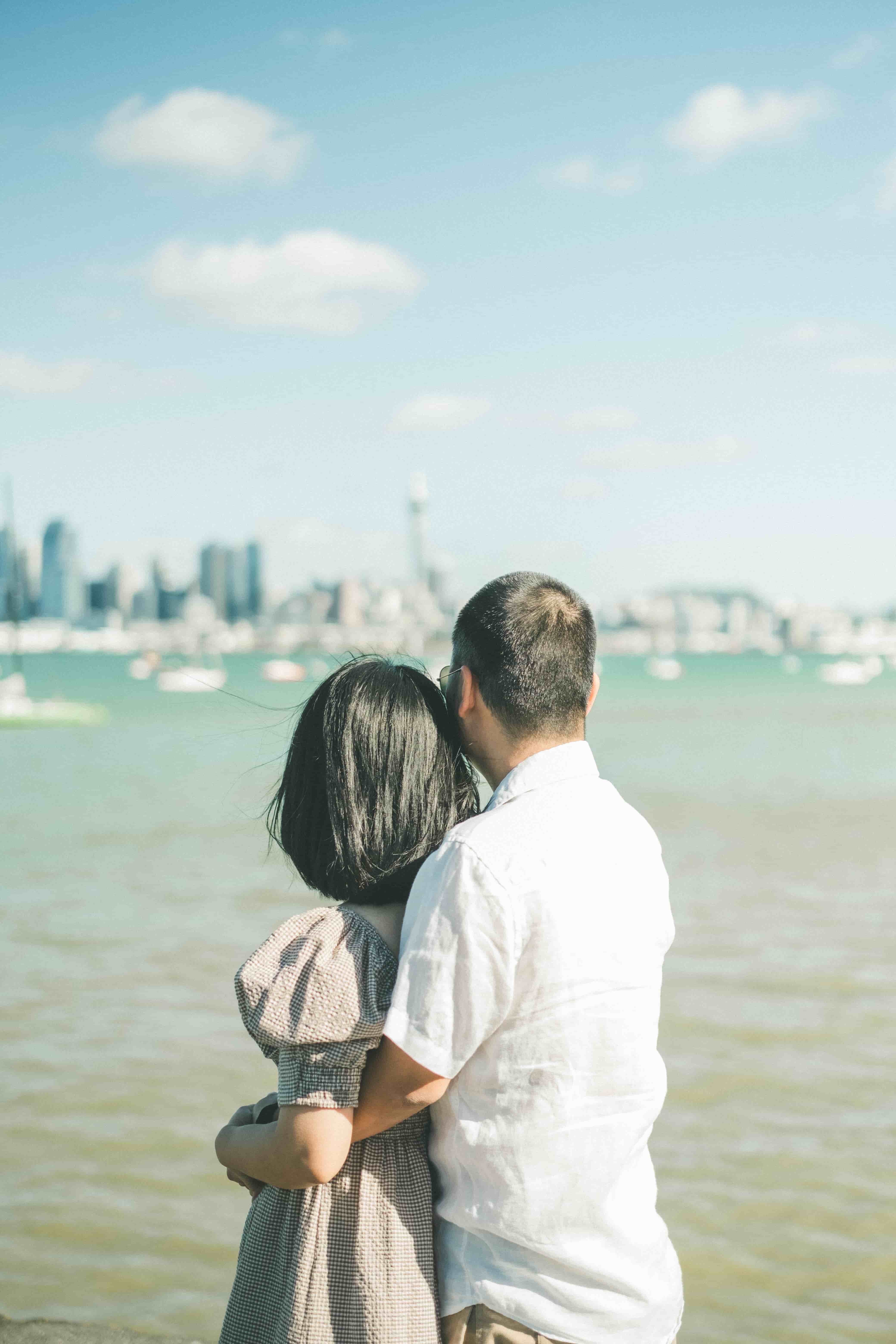Couple embracing at the water's edge with the Auckland skyline beyond