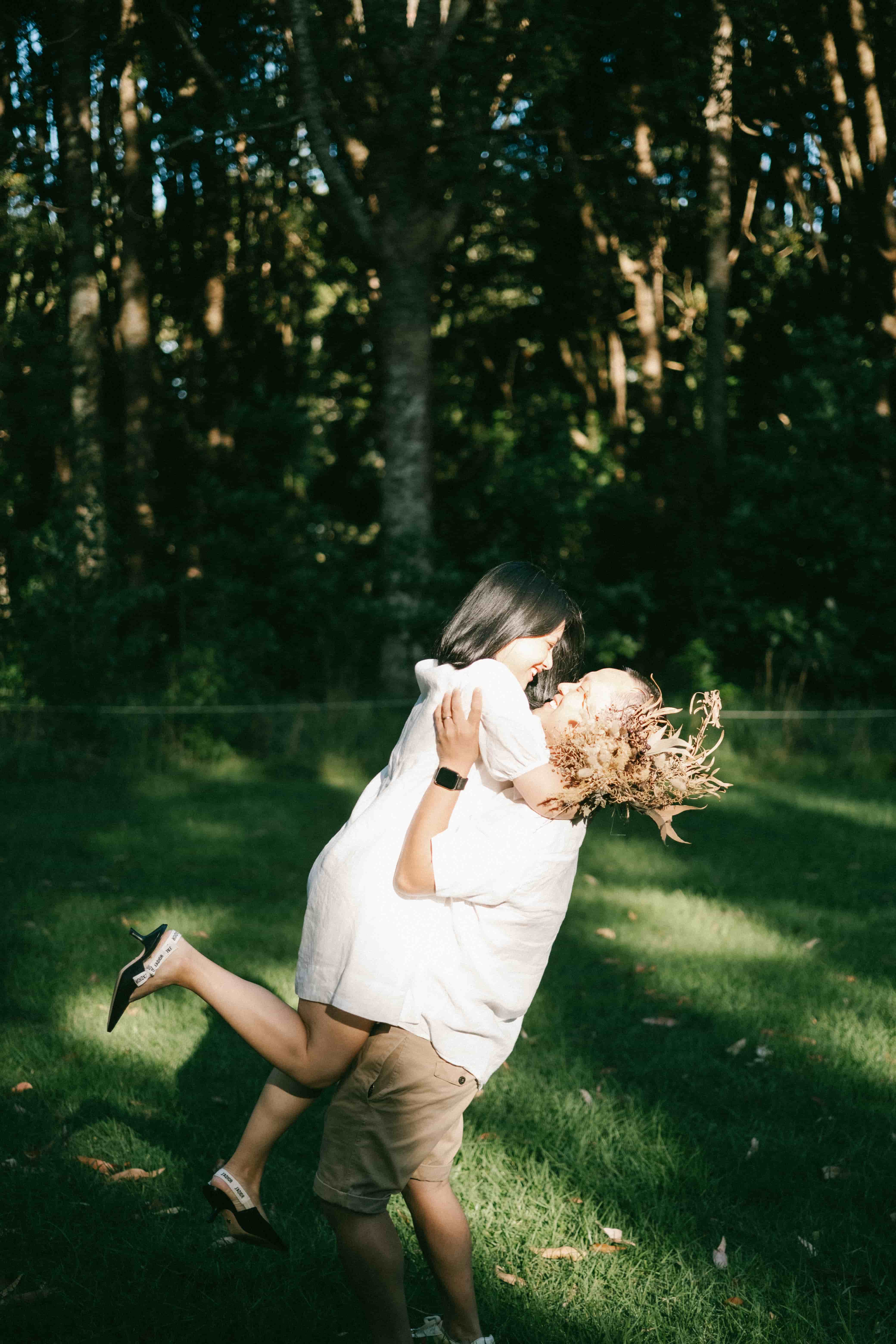 Husband lifting his wife off the ground in a sunlit clearing