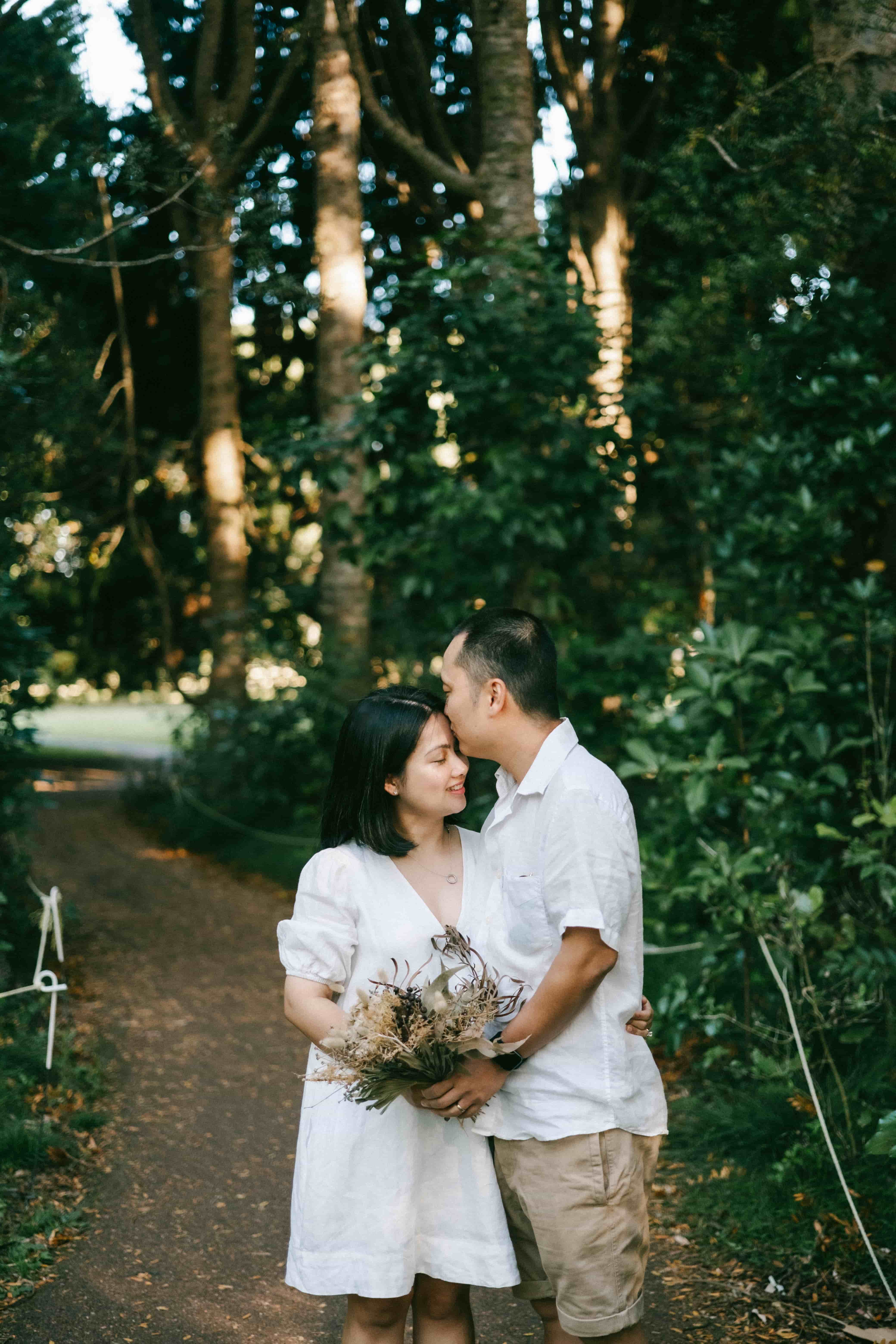 Husband kissing his wife's forehead on a forest path