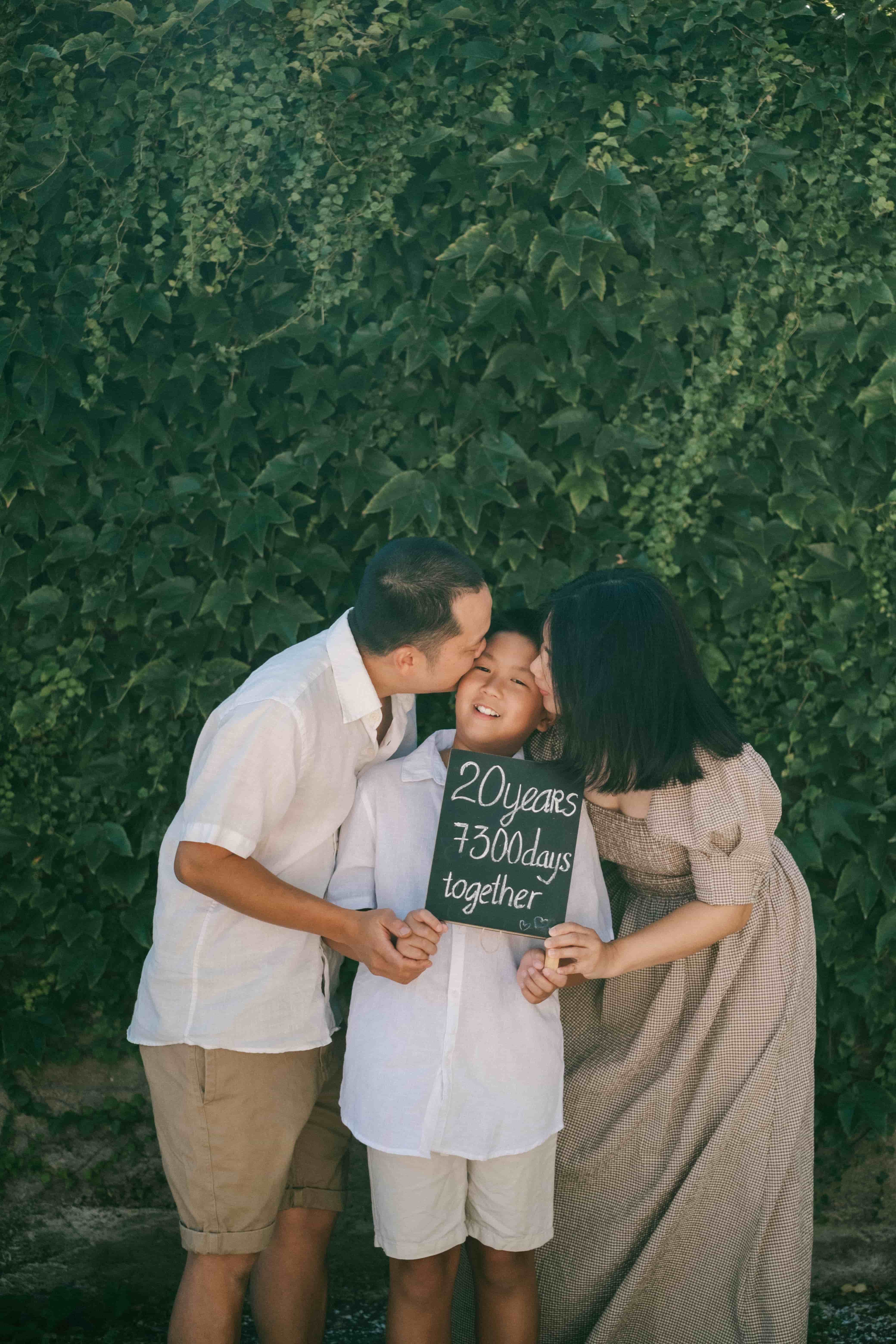 Parents kissing their son's cheeks as he holds a "20 years, 7300 days together" chalkboard