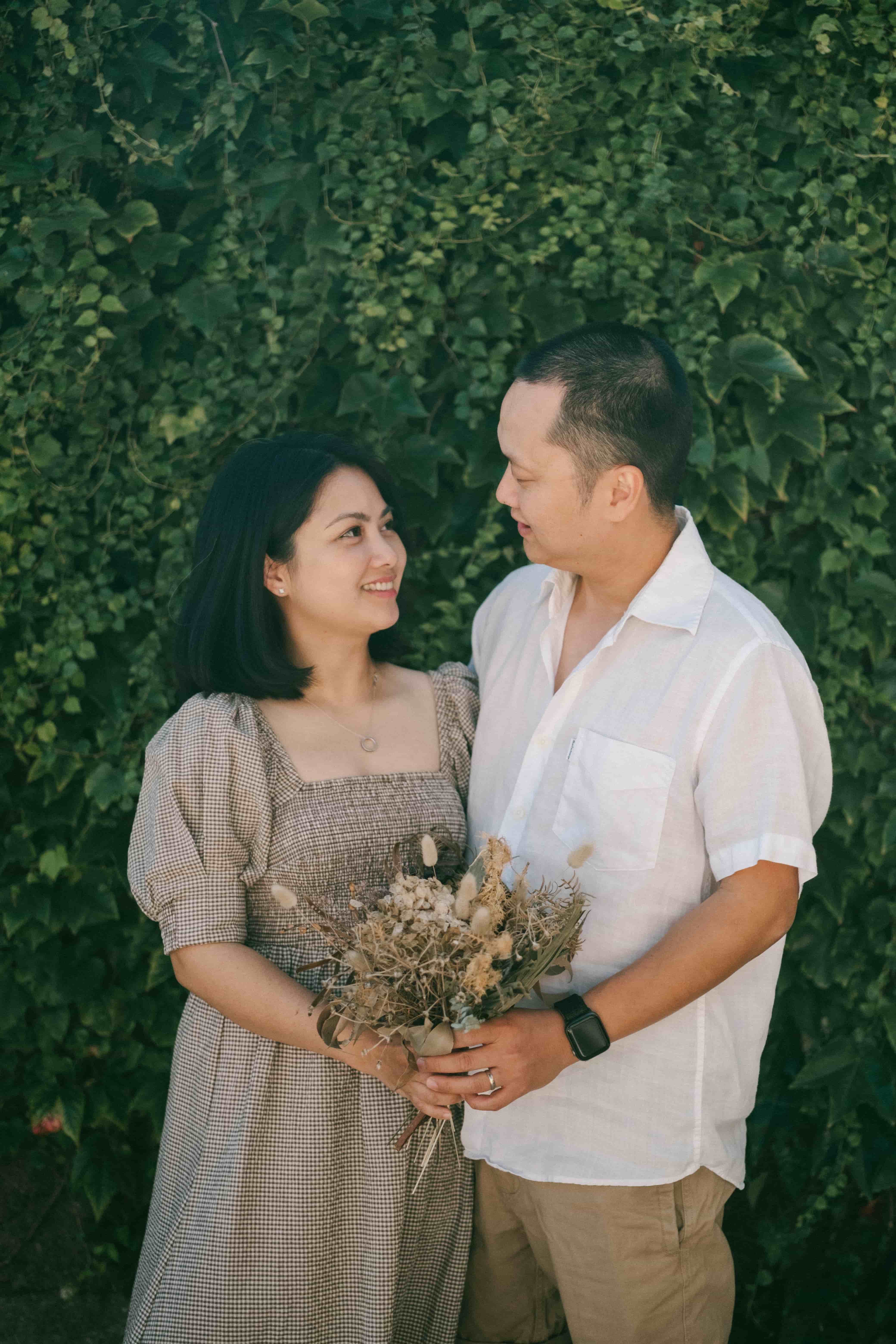 Couple holding a dried flower bouquet in front of an ivy wall