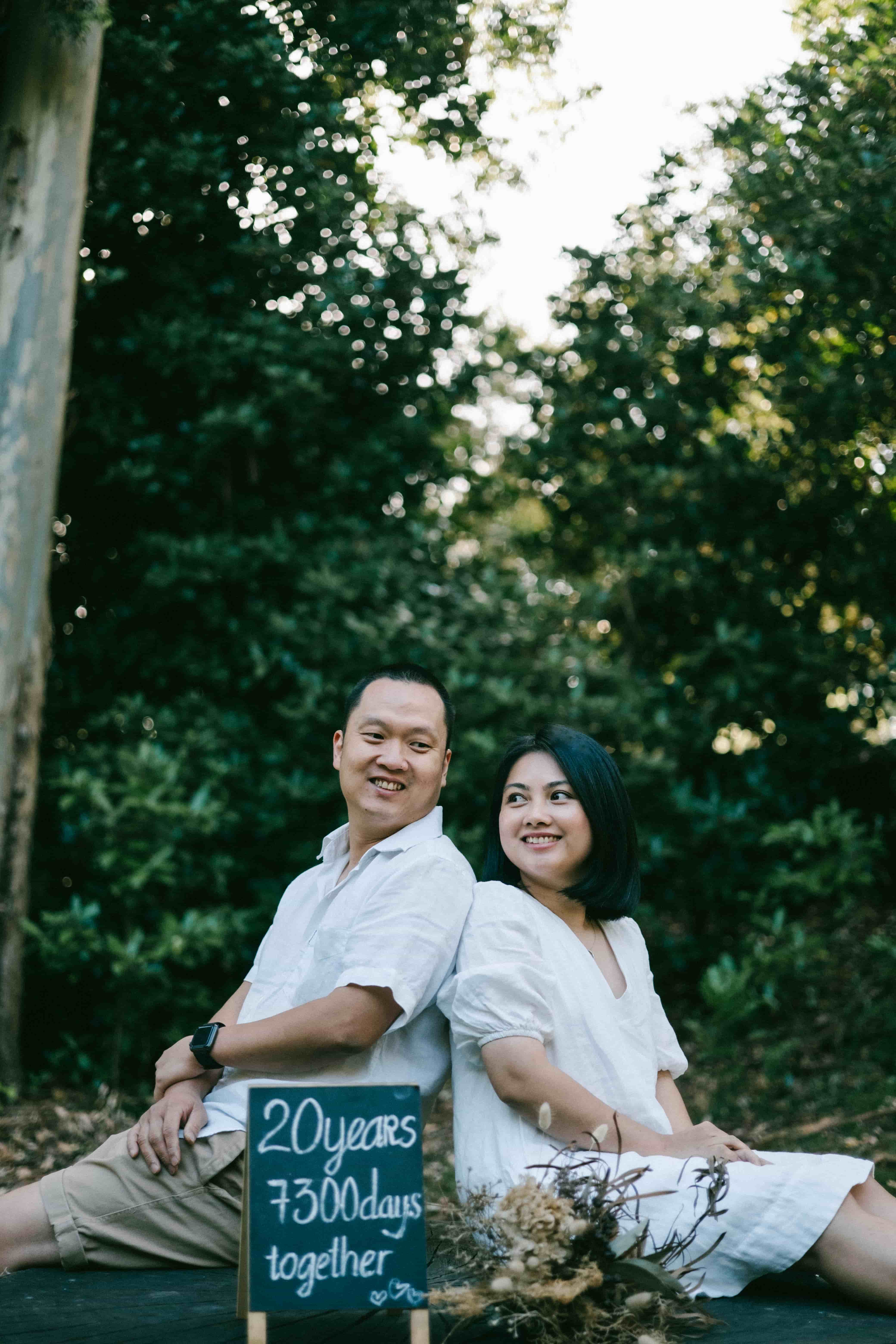 Couple smiling at the camera, sitting back to back on a stump