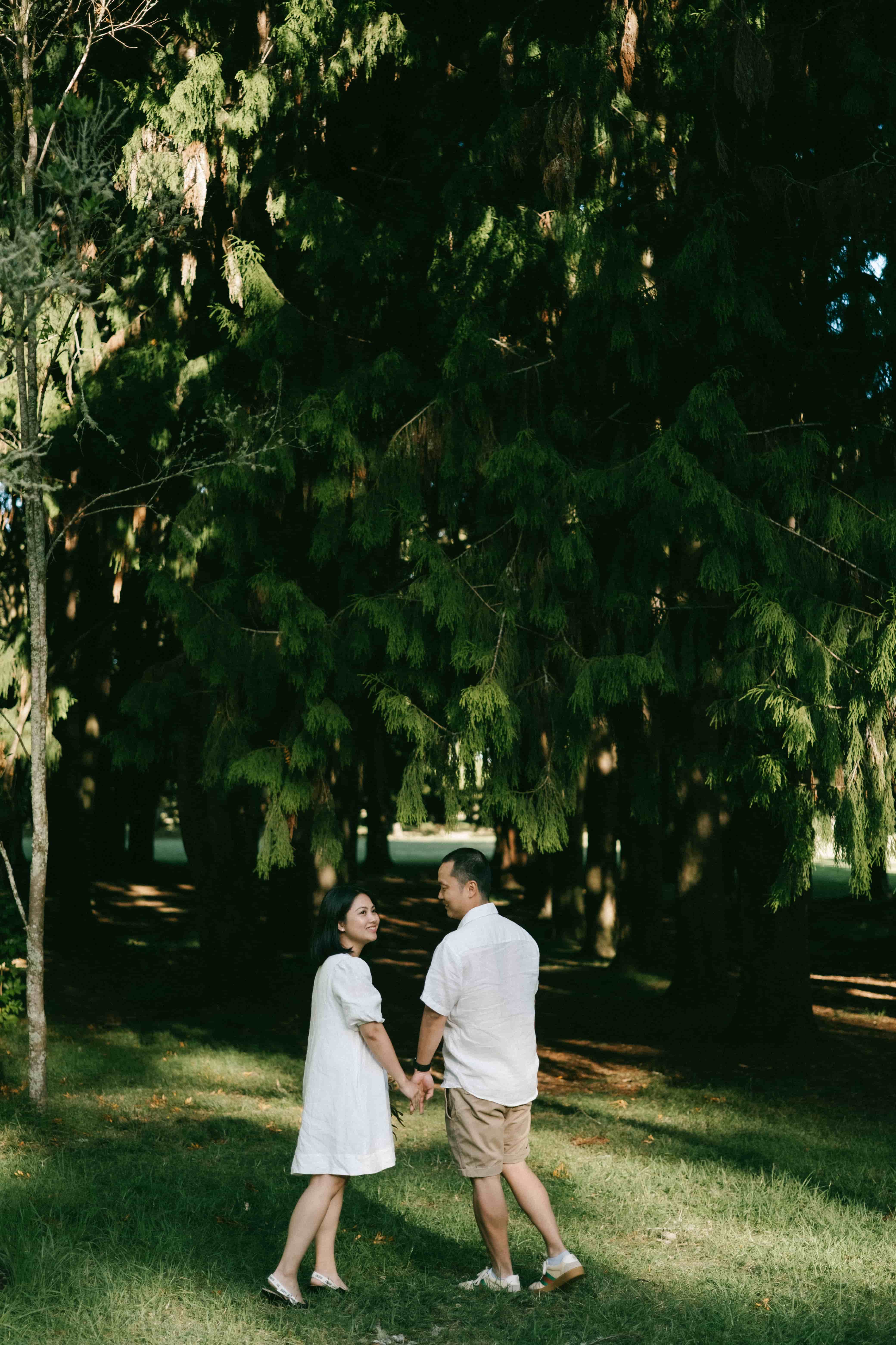 Couple walking hand in hand on the grass among tall pines