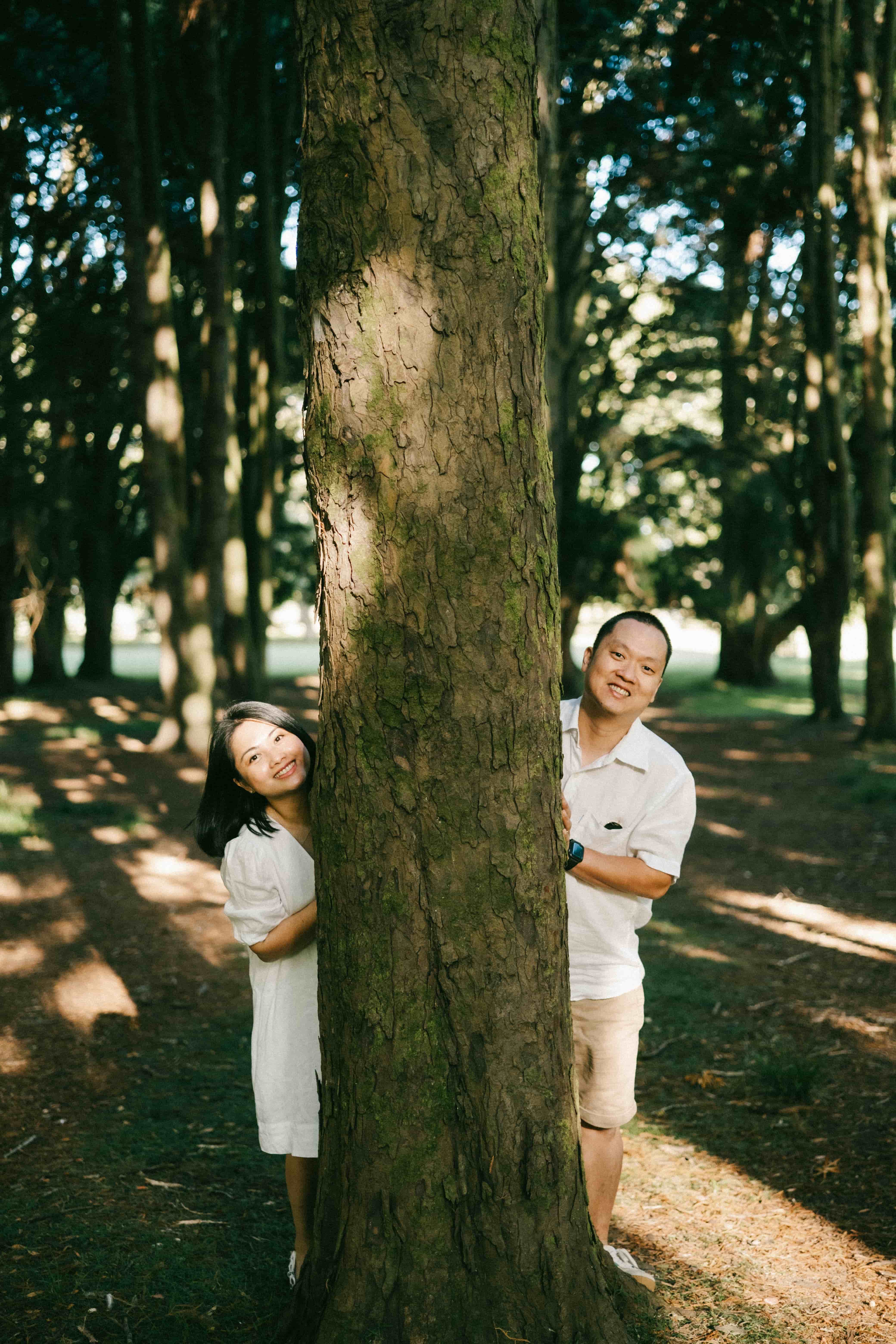 Couple peeking out from either side of a tall tree
