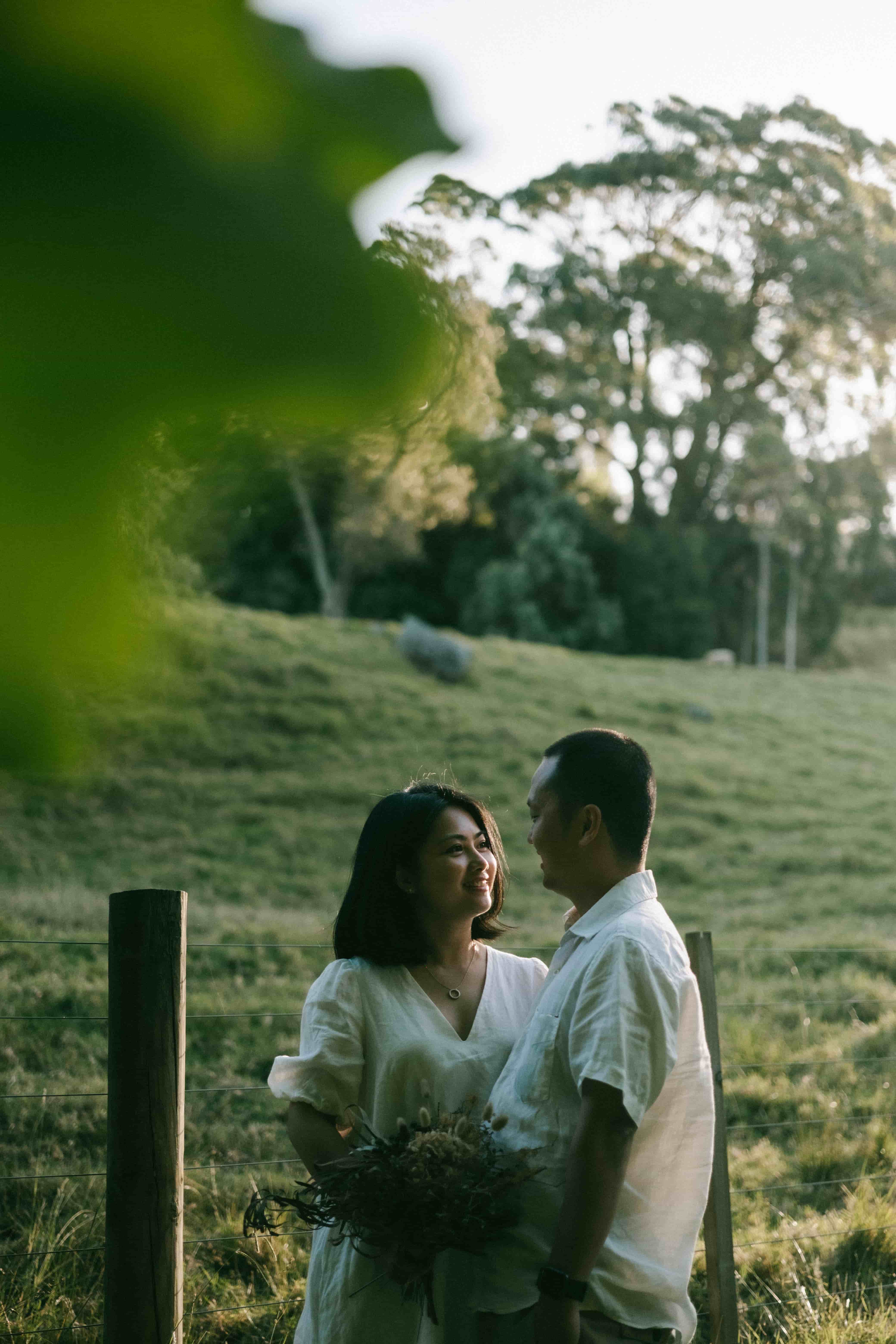 Couple embracing beside a fence post in a grassy paddock