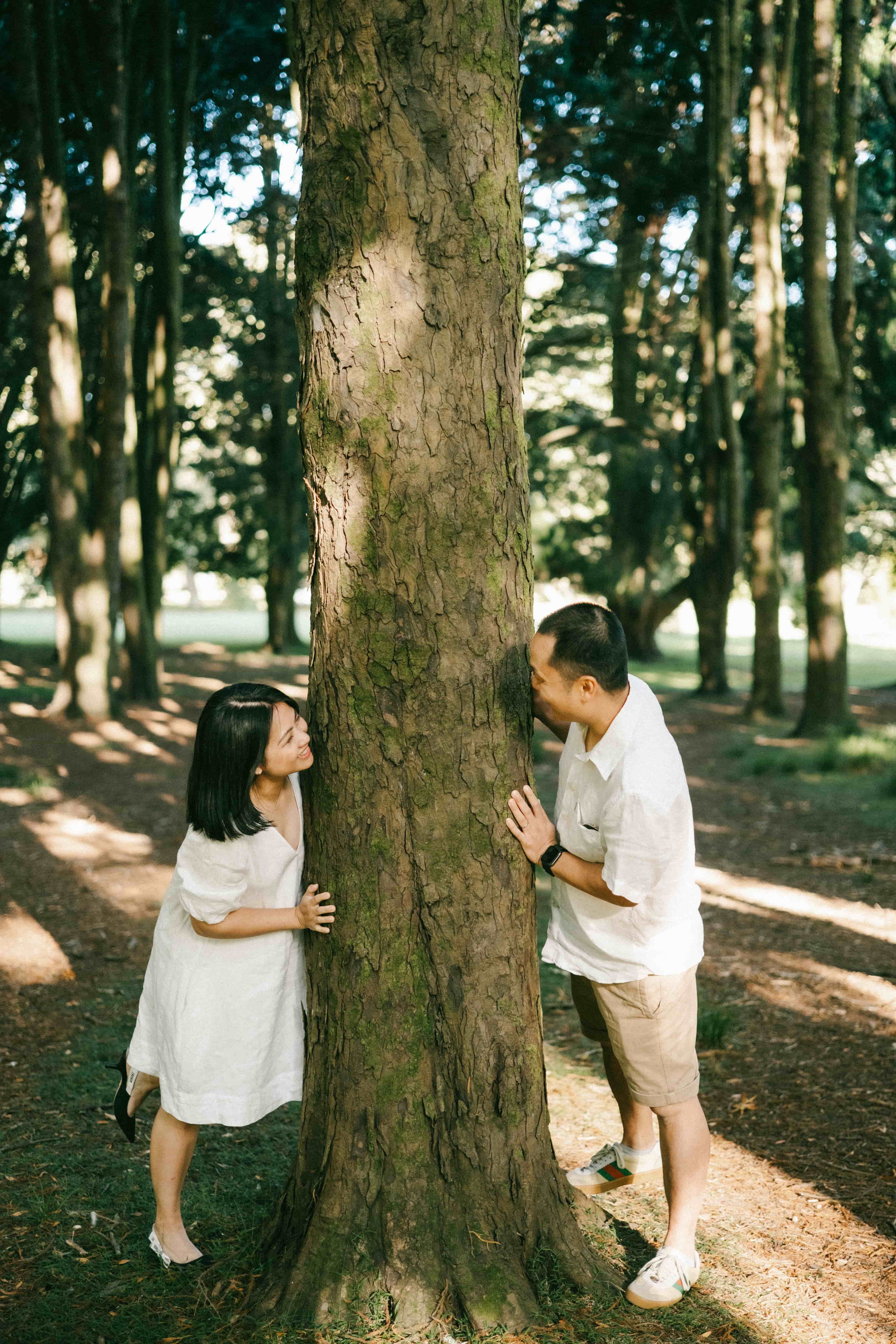 Couple leaning on opposite sides of a tree trunk