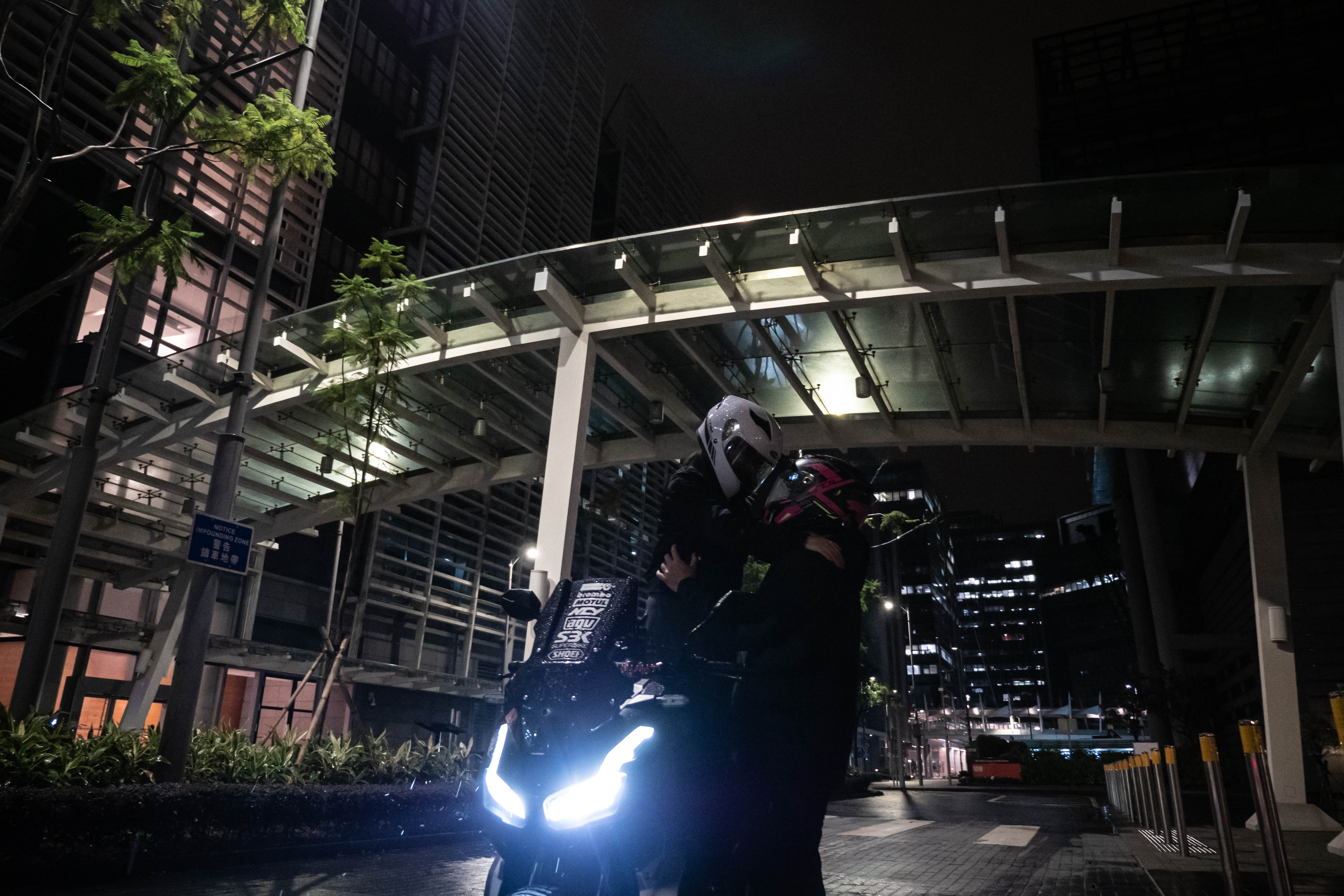 Two helmeted riders with the motorcycle under a curved canopy at night