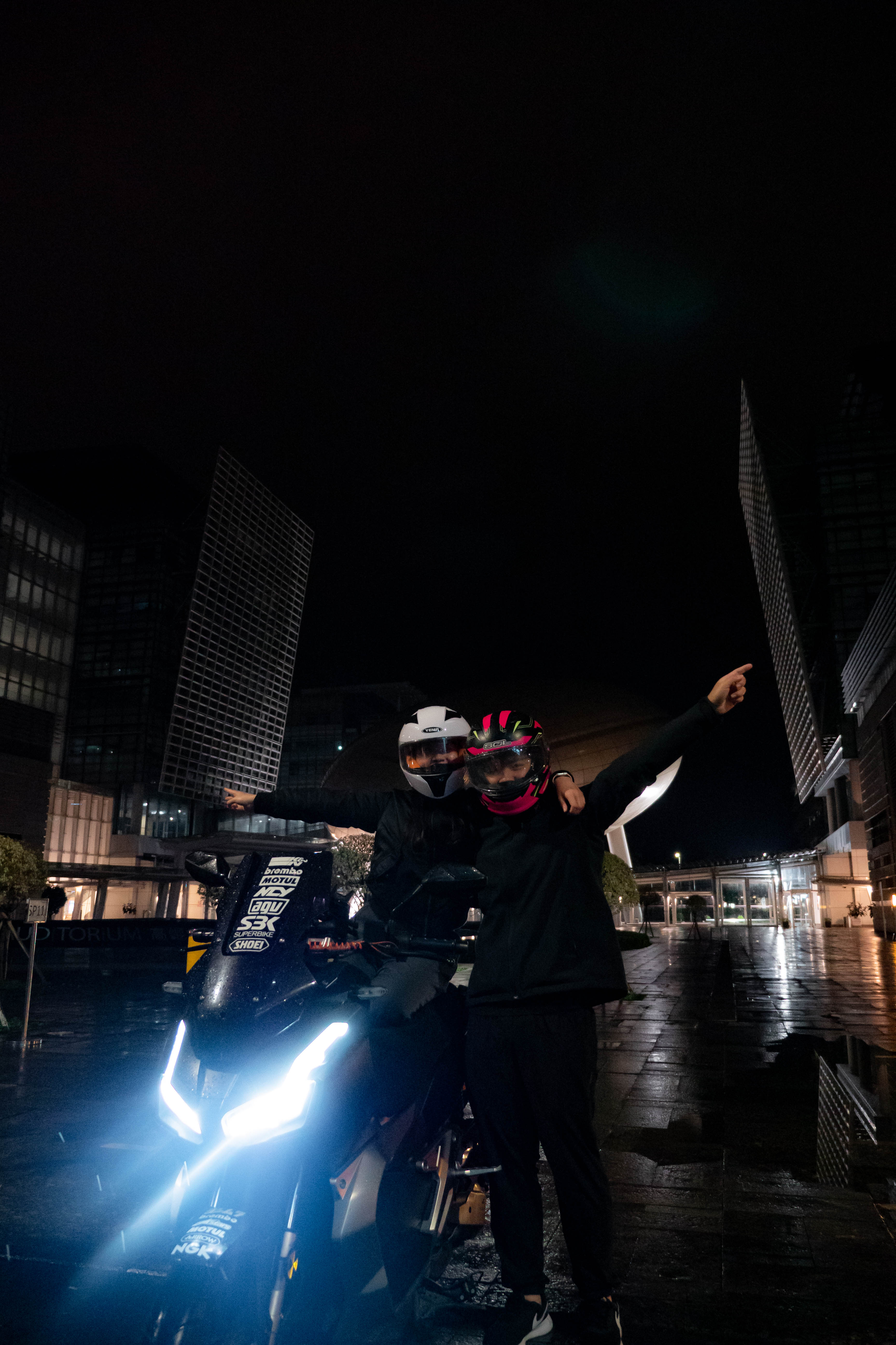 One rider pointing up at the towers beside the glowing motorcycle