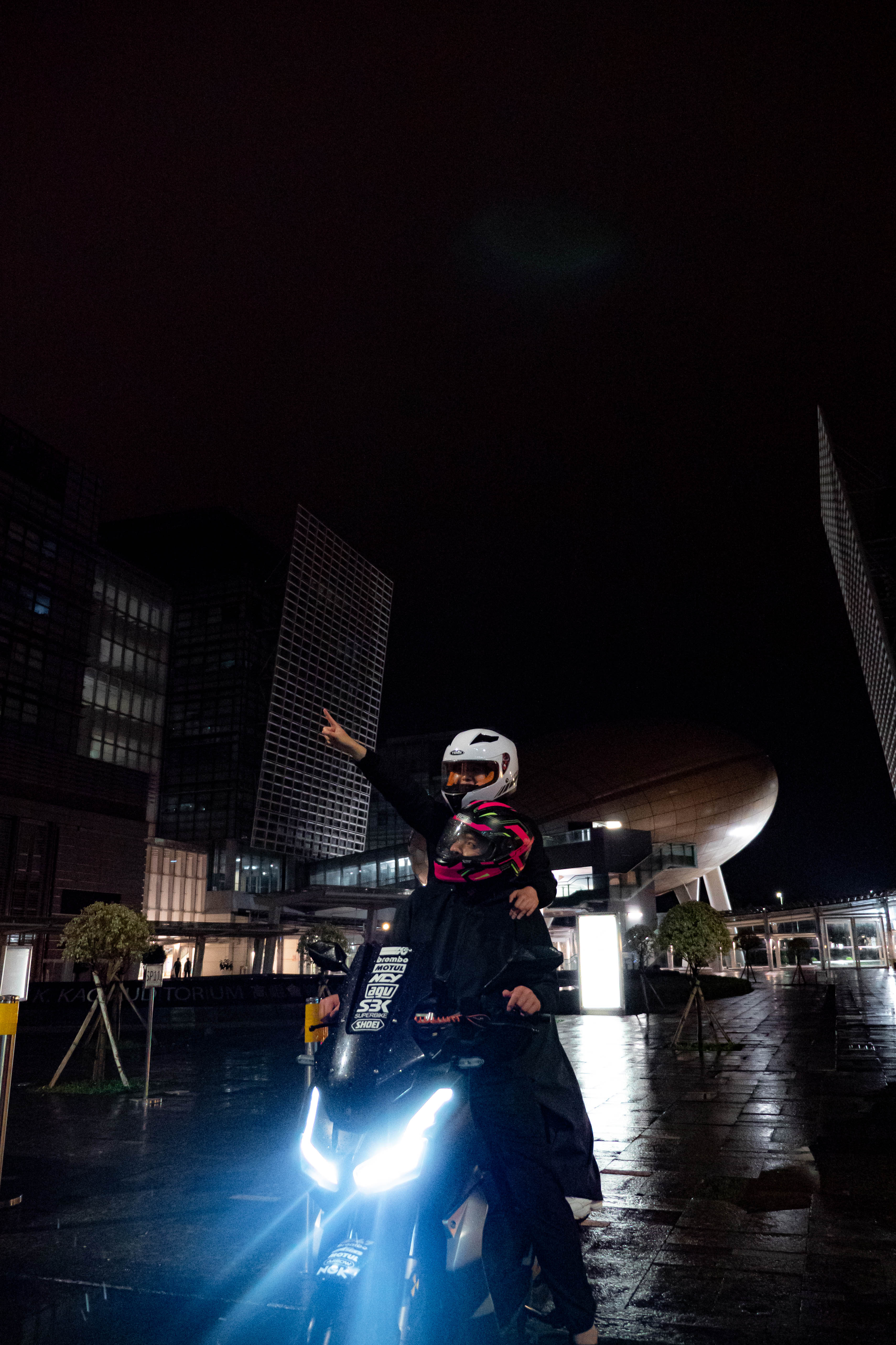Passenger raising an arm on the motorcycle in an empty wet plaza
